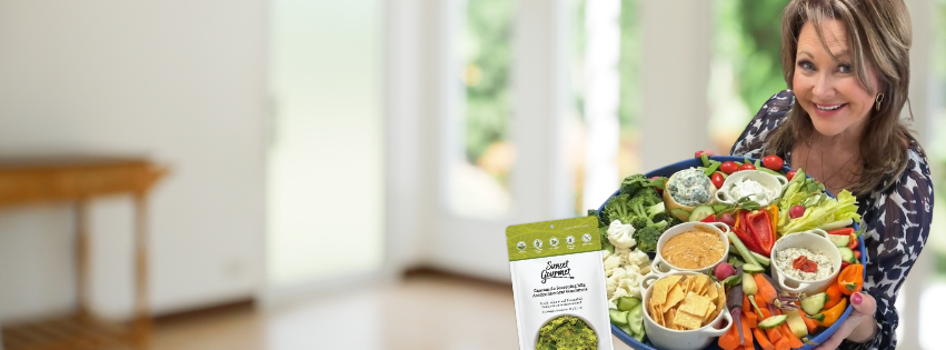 Woman holding a large bowl of assorted fresh vegetables, including cherry tomatoes, broccoli, and carrots, in a bright room with a door or window in the background. Jacqueline with Appetizer Platter