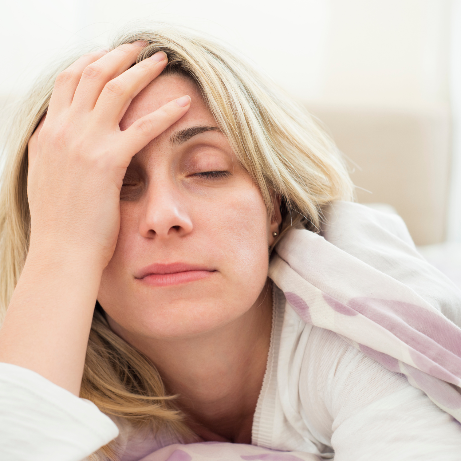 A woman with blonde hair rests her hand on her forehead with her eyes closed.