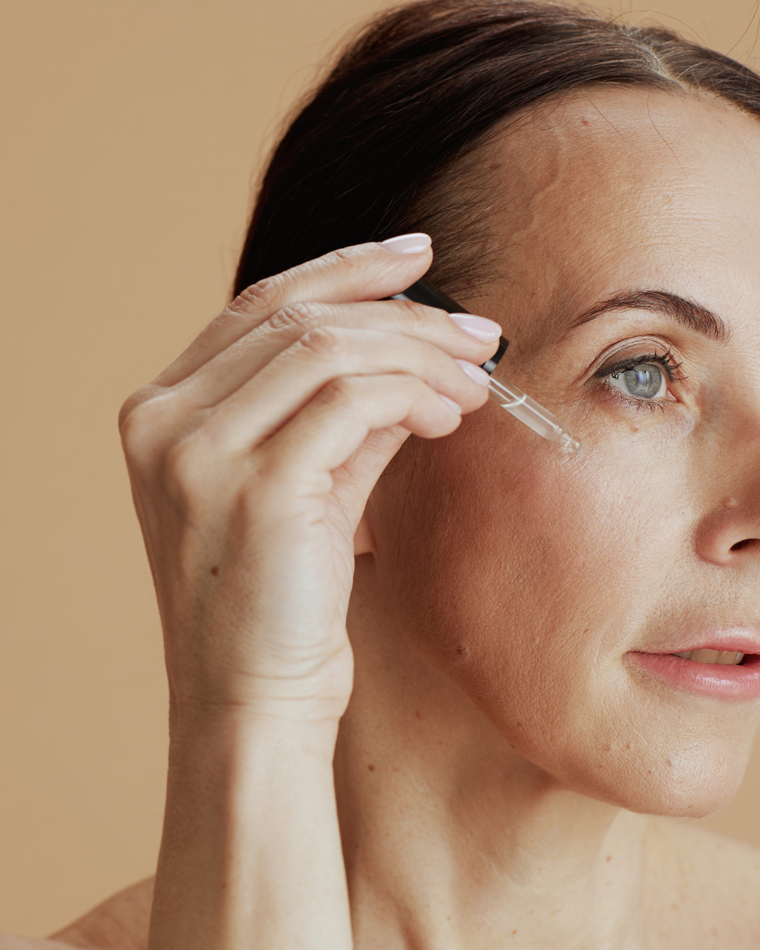 A woman applying skincare serum under her eye using a dropper.