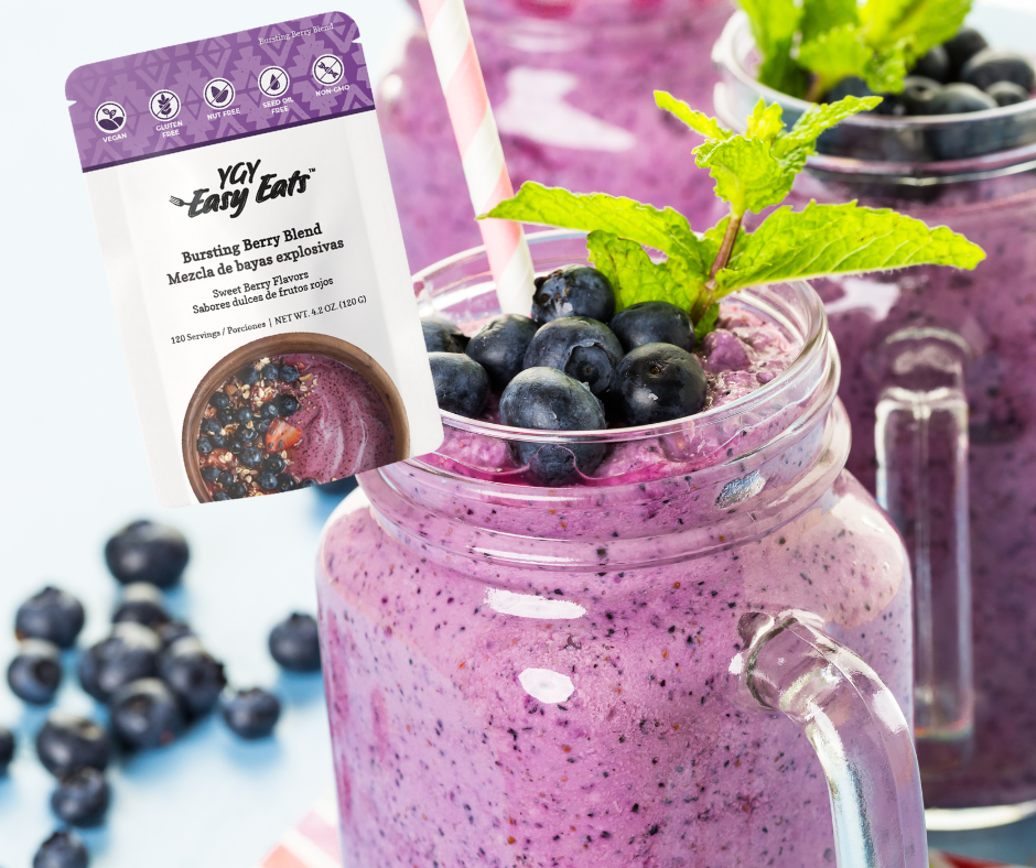 Two glass mason jar drinks with purple blueberry smoothies topped with fresh blueberries and mint leaves, with a pink and white striped straw, and a package of Bursting Berry Blend smoothie mix in the foreground.