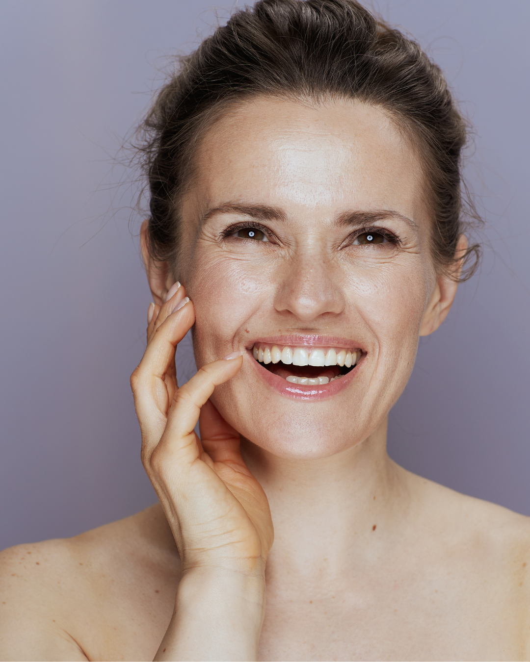 A woman smiling and touching her face with her hand, showing her teeth.