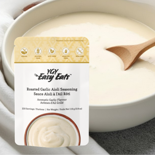 A bowl of creamy white sauce with a wooden spoon, labeled 'Roasted Garlic Aioli Seasoning' by YAY Easy Eats, with icons indicating it is vegan, gluten-free, nut-free, seed oil-free, and non-GMO.