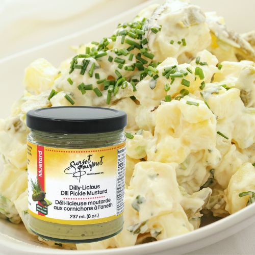 Potato salad topped with chopped chives and a dollop of sour cream in a white dish, with a jar of sweet gourmet dill pickle mustard in the foreground.