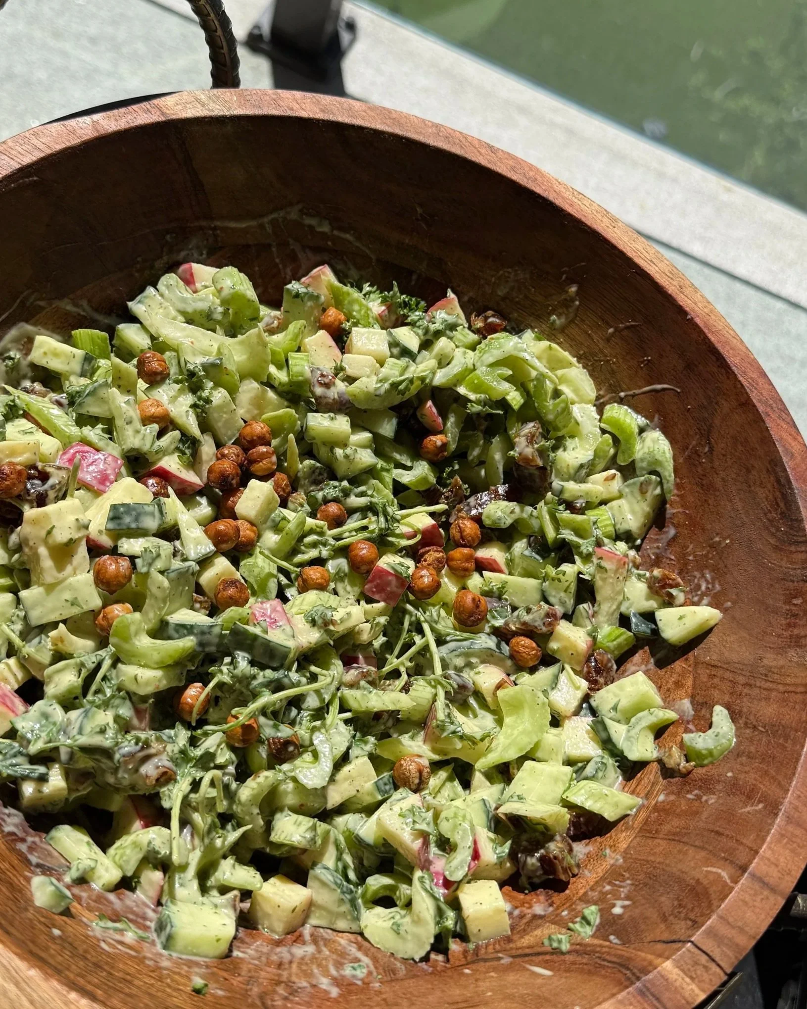 A bowl of potato salad with chopped celery, apples, kale, and whole peppercorns in a wooden bowl.