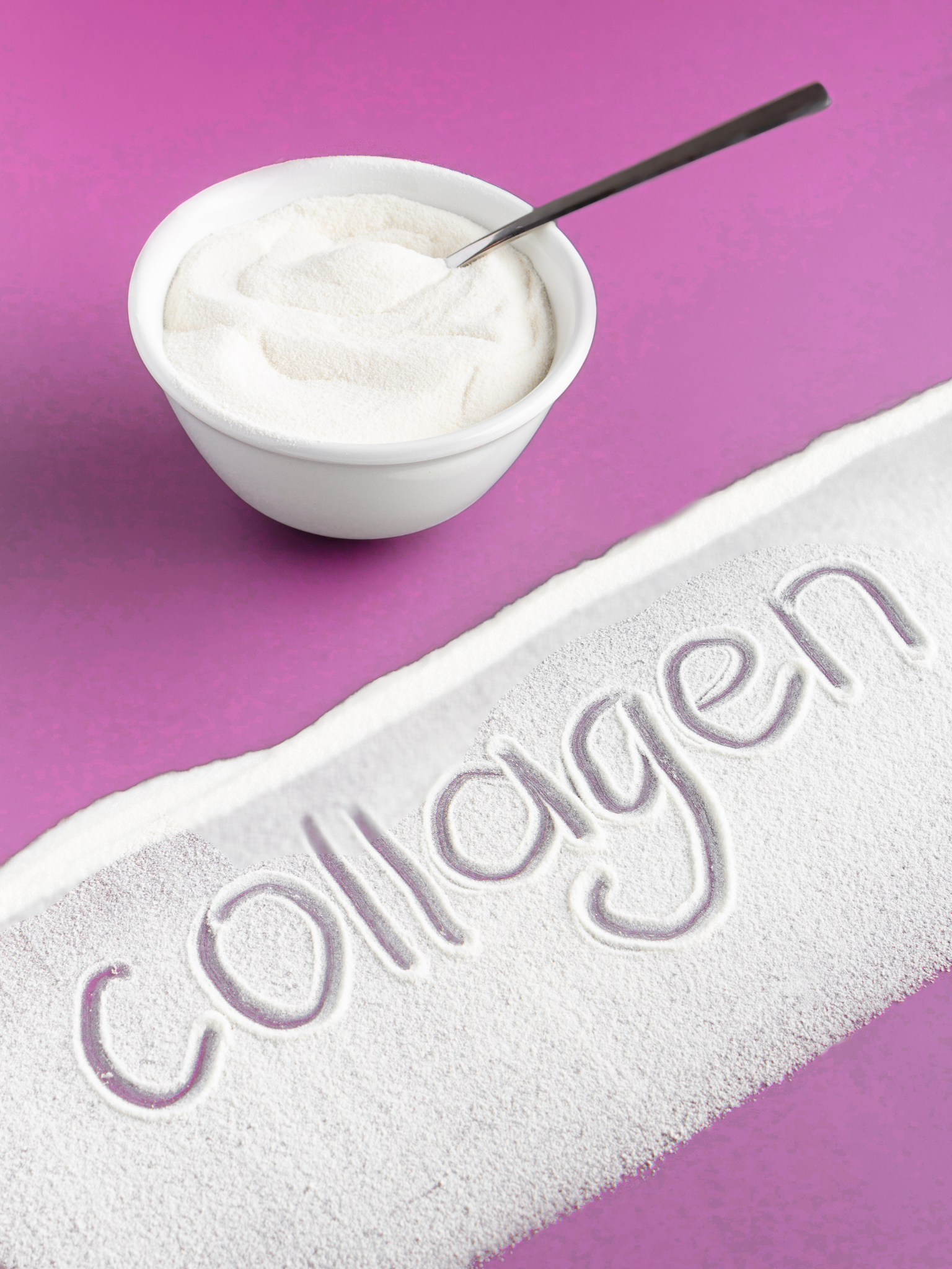 Close-up of white powder with a word 'care' written in the powder, on a pink background with a white bowl filled with powder and a spoon.