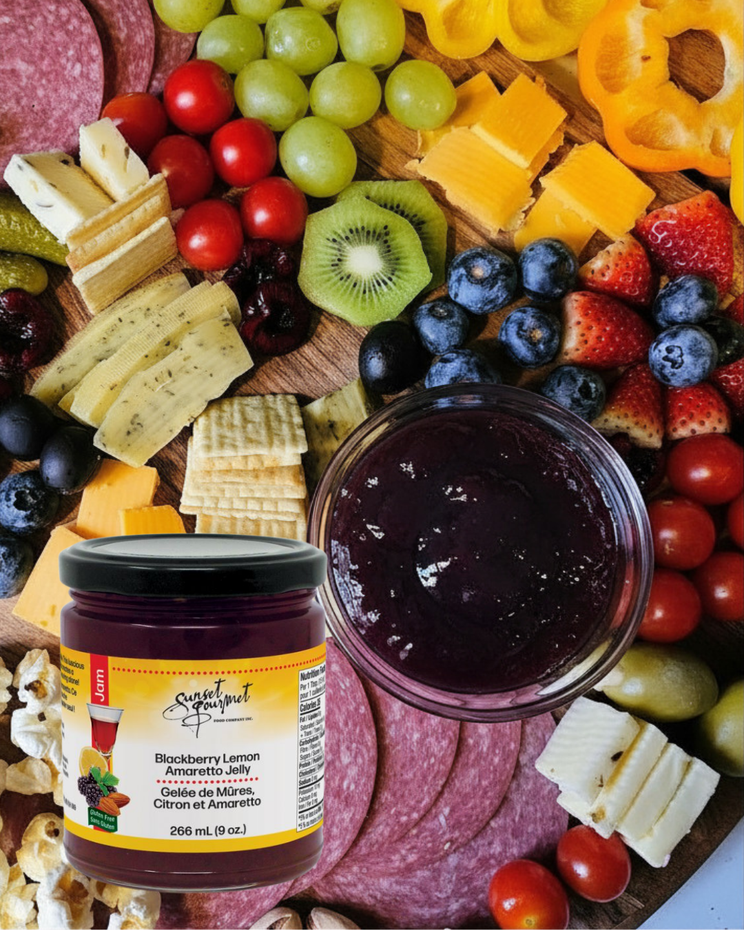 A variety of sliced and whole fruits including cherry tomatoes, grapes, strawberries, blueberries, kiwi, yellow and red bell peppers, and cheese, with a jar of blackberry lemon amaretto jelly in front.