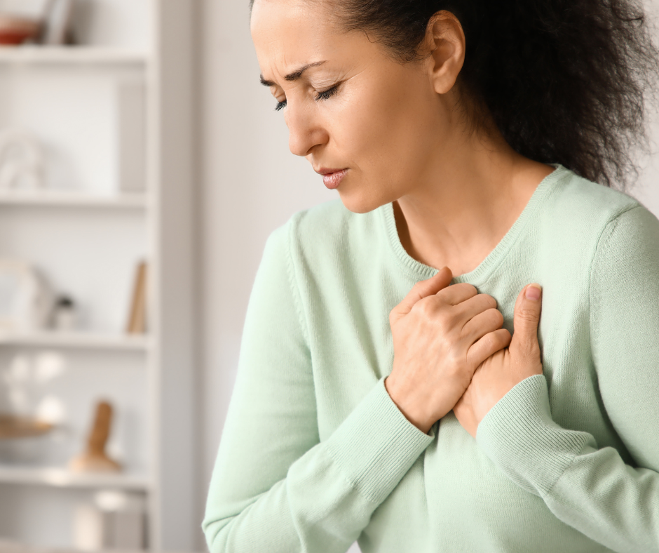 Woman clutching her chest, appearing to experience chest pain or difficulty breathing in a home setting.
