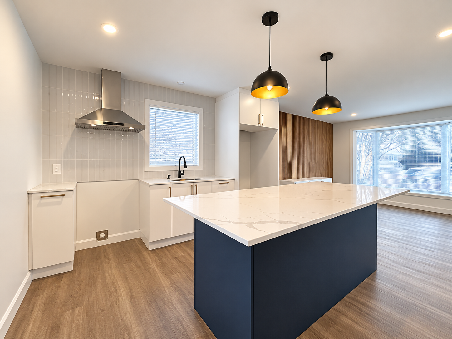 Bright open-concept kitchen renovated by Garcia Construction Rénovation in Quebec City, featuring white cabinetry, a contrasting navy island and window above the sink. 