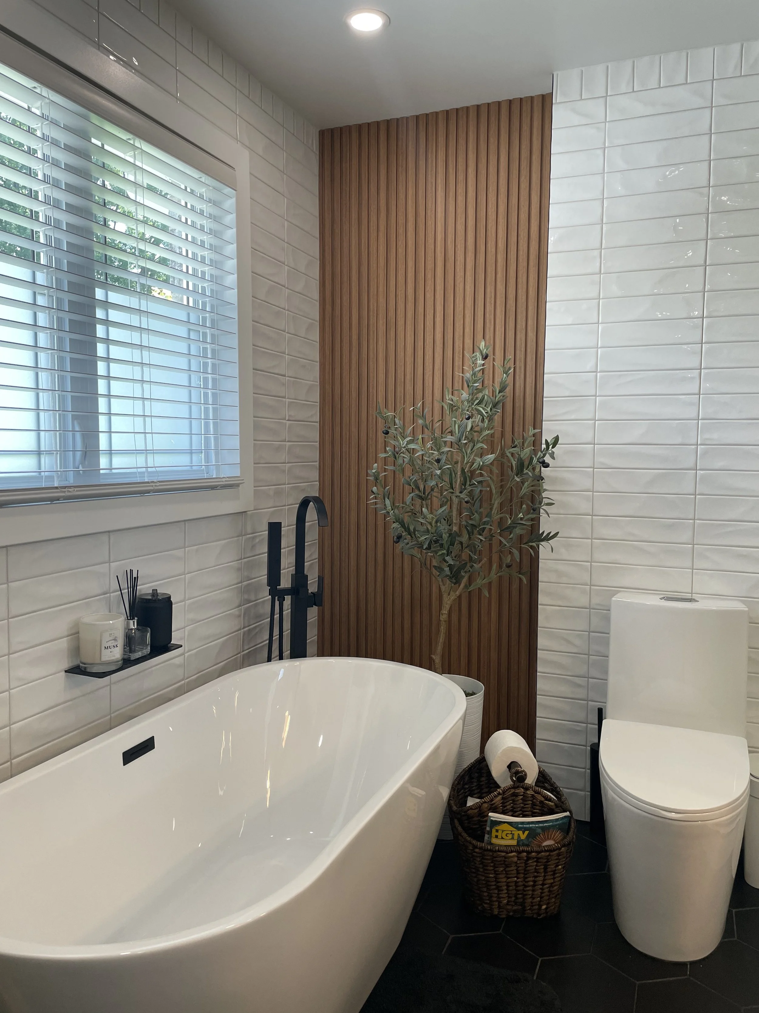 Bathroom renovation by Garcia Construction Rénovation in Quebec City with a freestanding bathtub, wood accent wall, black fixtures and window above the bathtub.