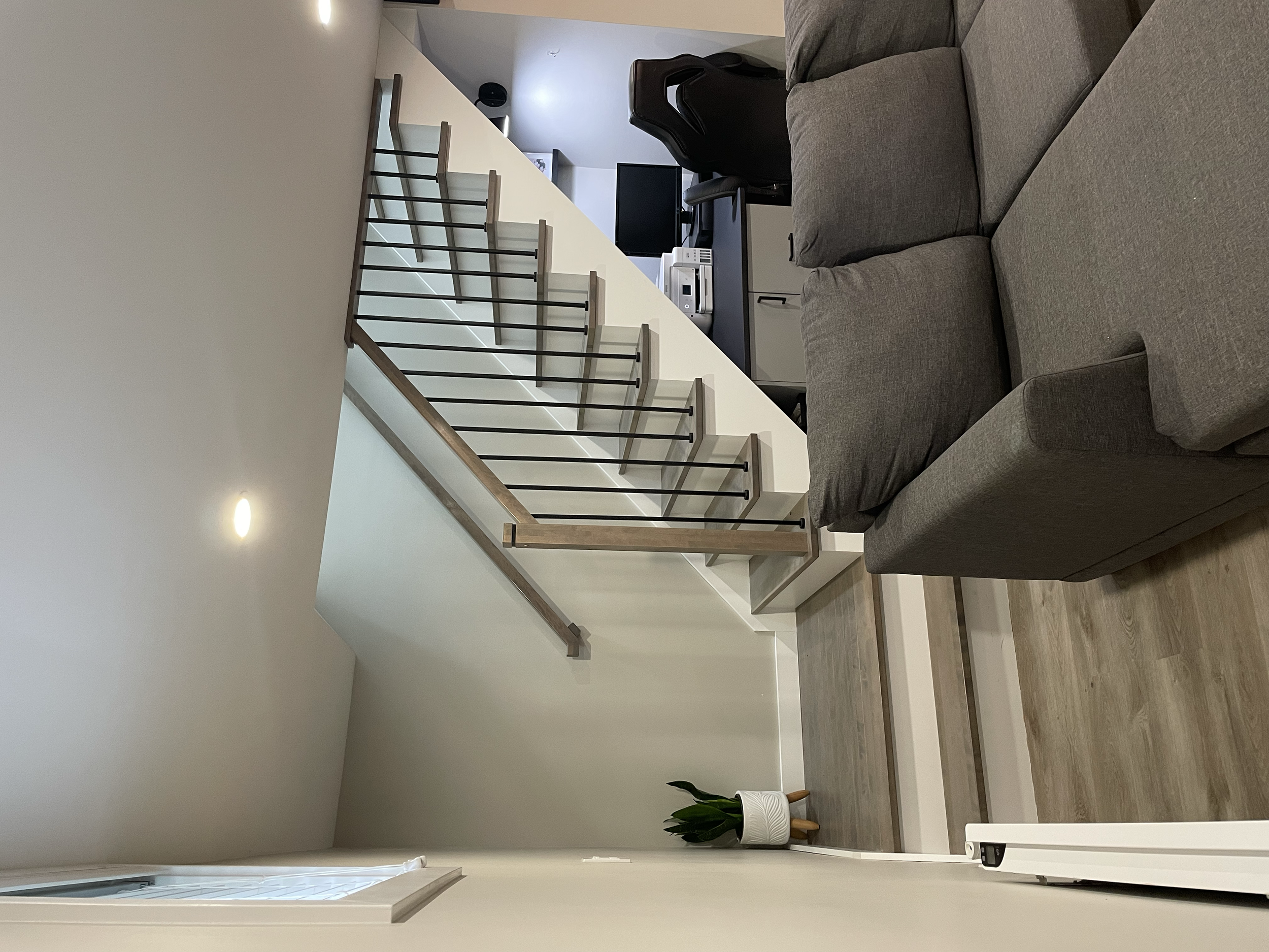Rénovation de sous-sol réalisée par Garcia Construction Rénovation à Québec, avec escalier moderne à rampe noire, espace bureau sur mesure sous l’escalier et finitions contemporaines aux tons neutres.