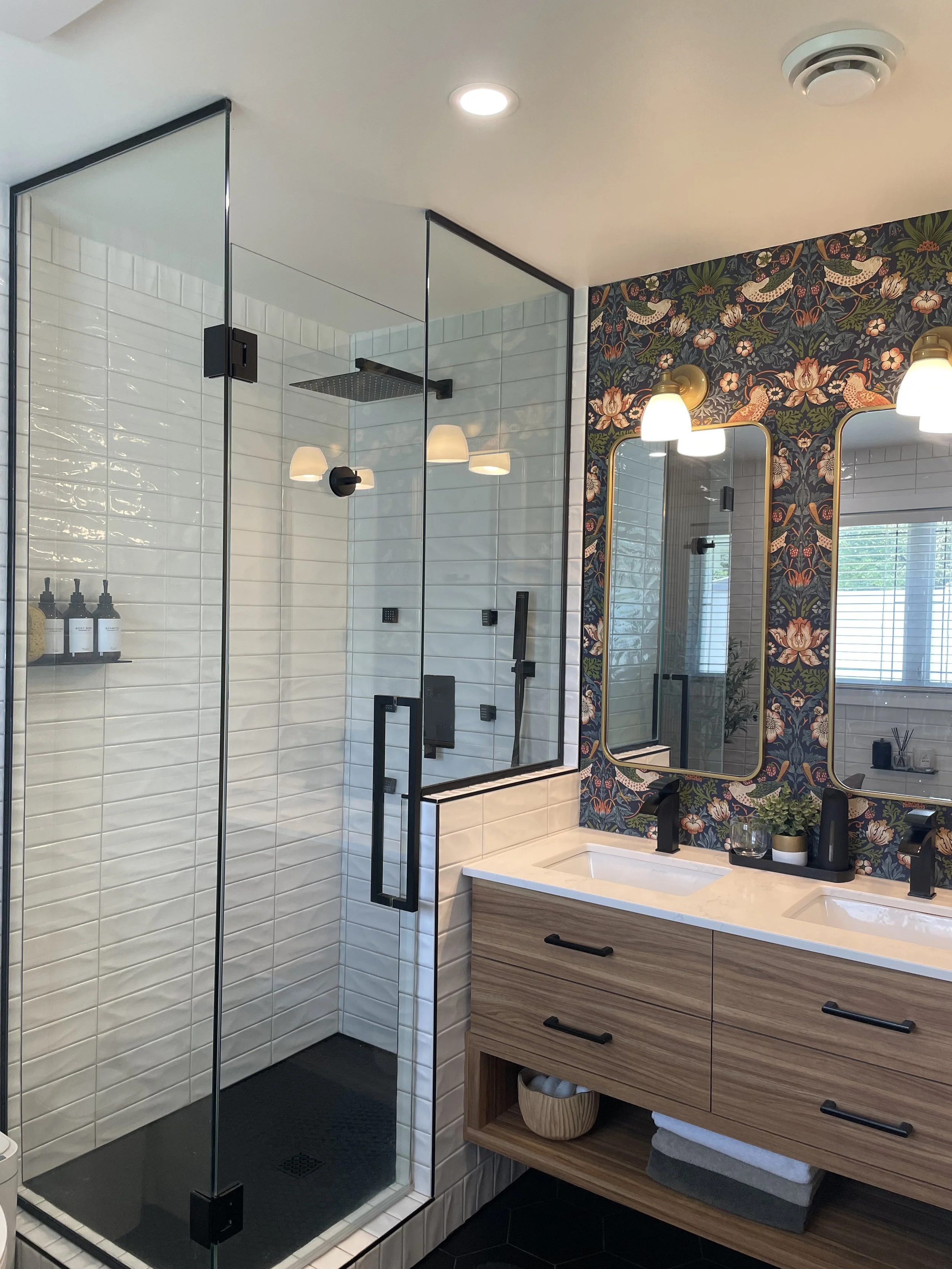 Rénovation de salle de bain réalisée par Garcia Construction Rénovation à Québec, avec douche en verre, vanité double en bois, carrelage blanc et papier peint floral.
