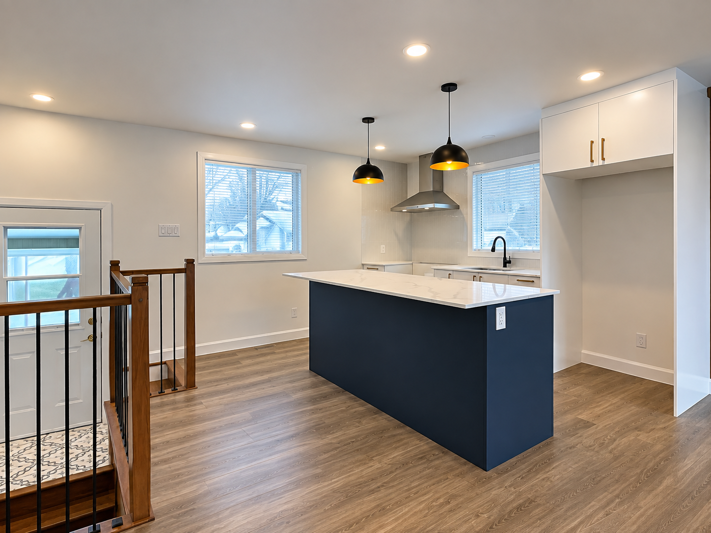Bright open-concept kitchen renovated by Garcia Construction Rénovation in Quebec City, featuring white cabinetry, a contrasting navy island and window above the sink. 