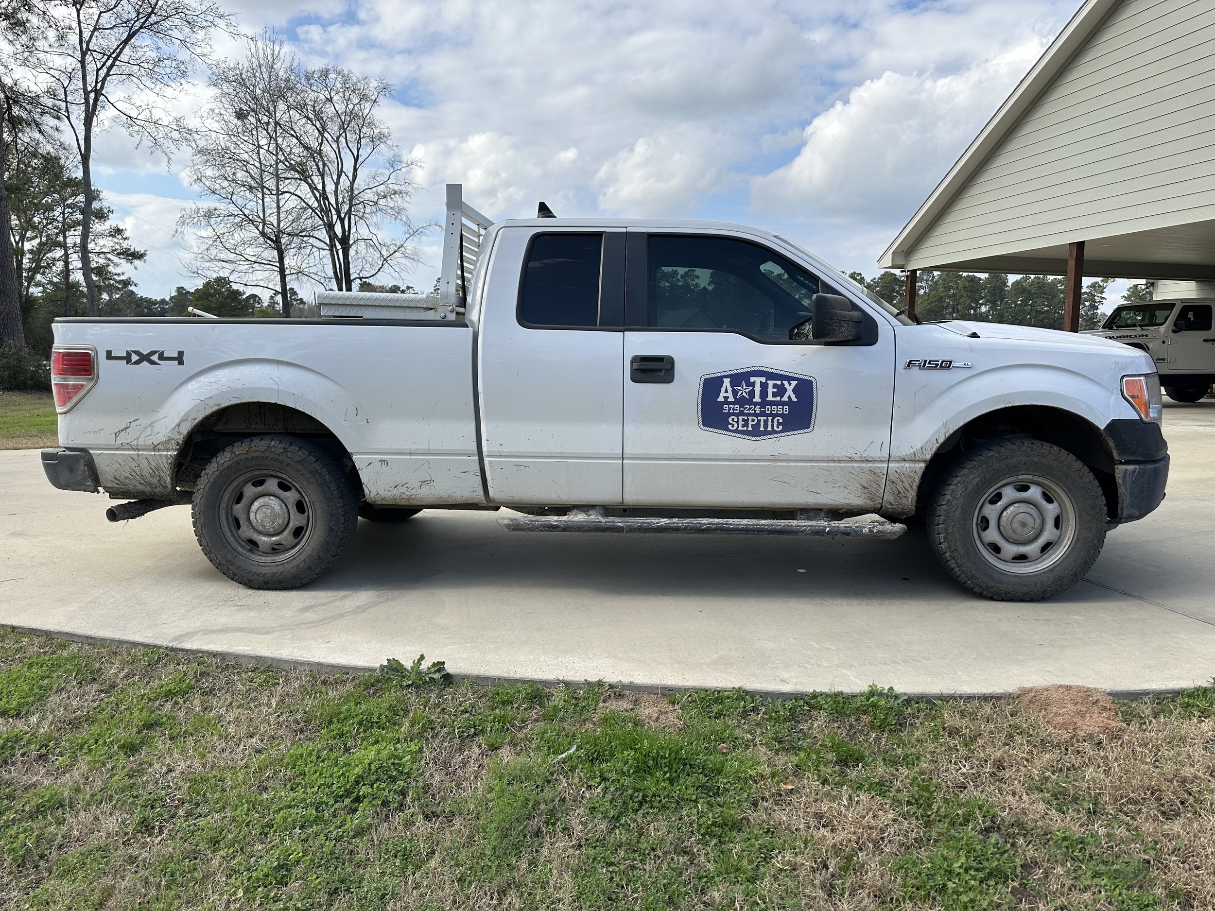 A white pickup truck with a decal on the door that reads 'A TEX SEPTIC' parked in front of a carport.