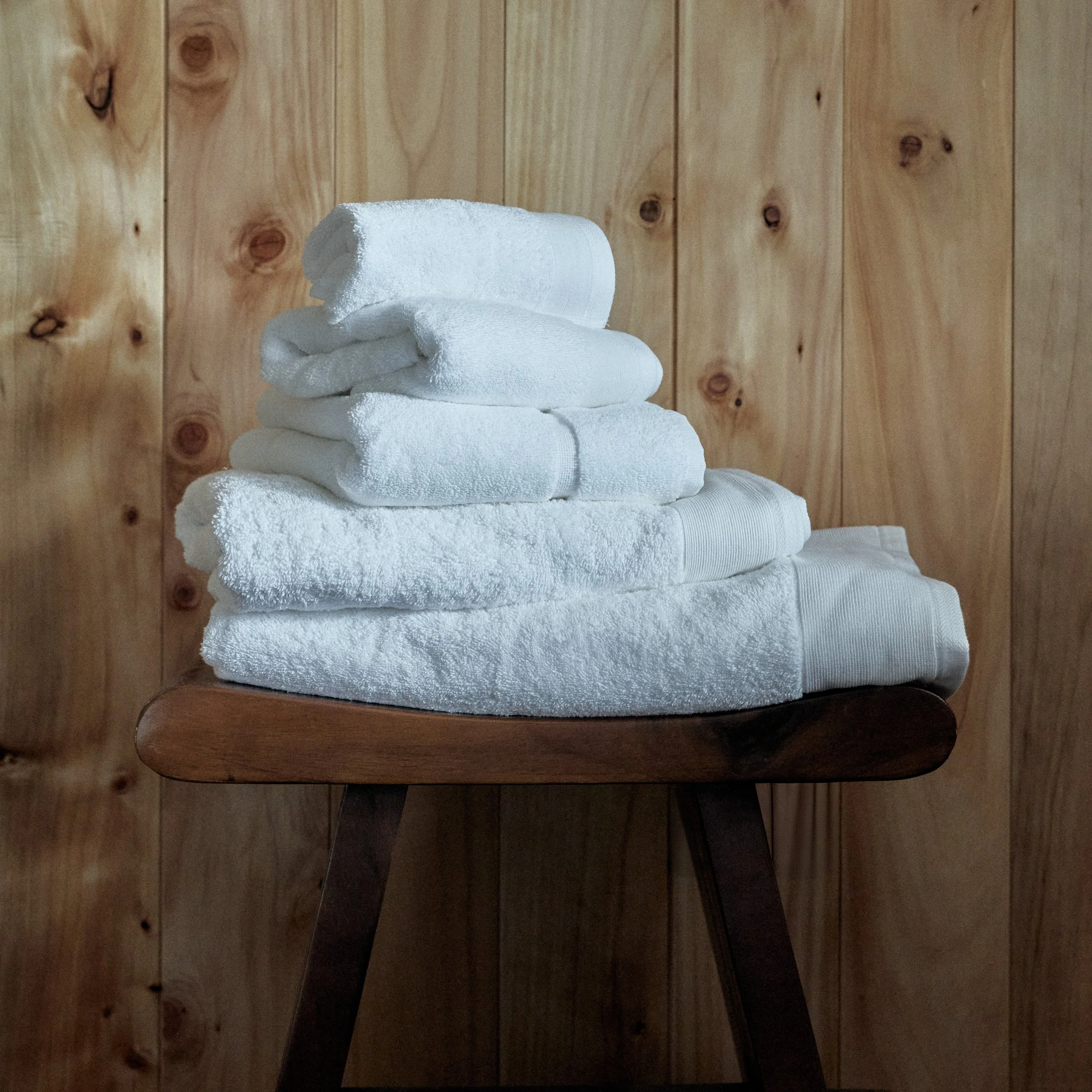 Stack of white towels on a dark wooden chair in front of a wood-paneled wall.