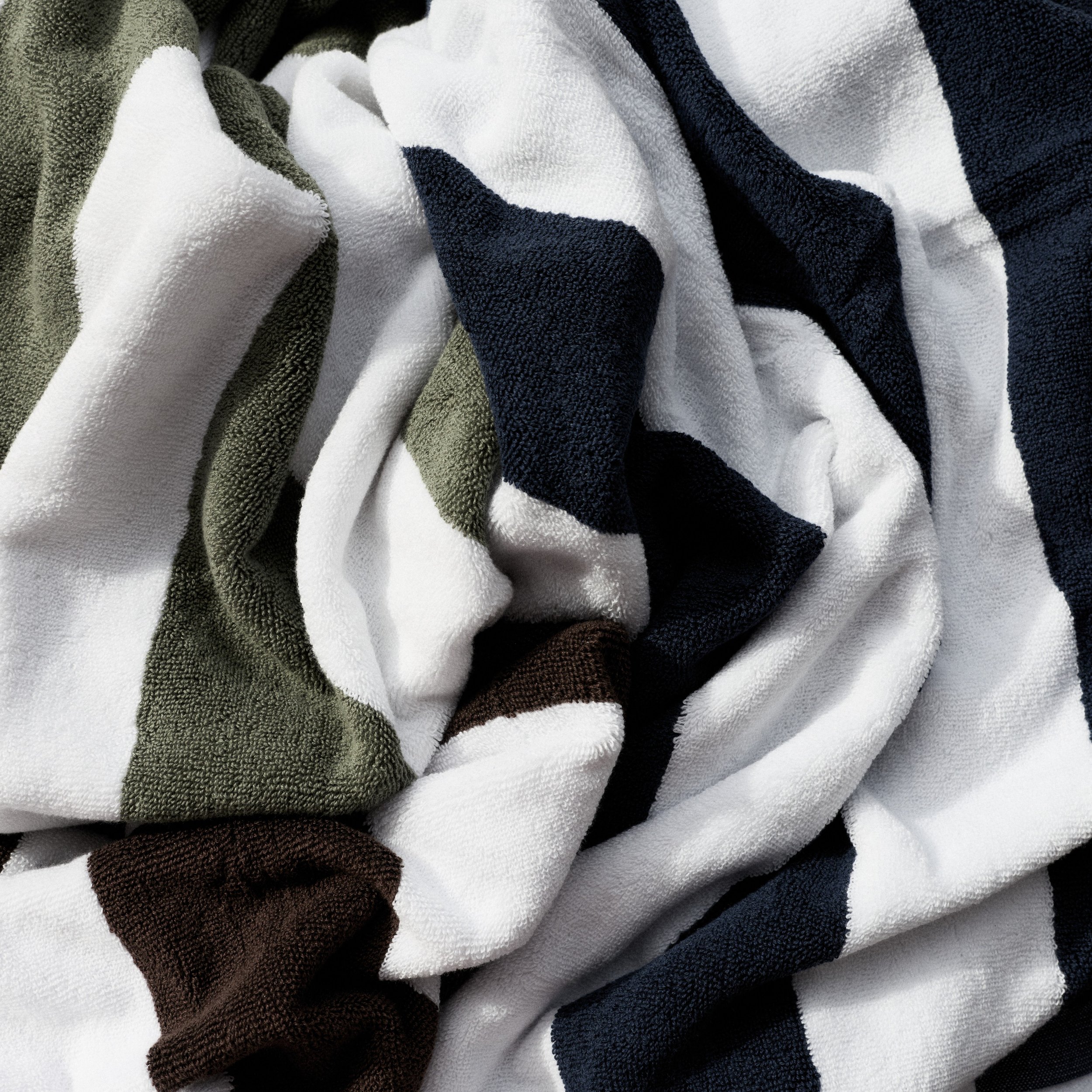 Close-up of folded, textured beach towels in colors including white, black, olive, brown, and dark green.
