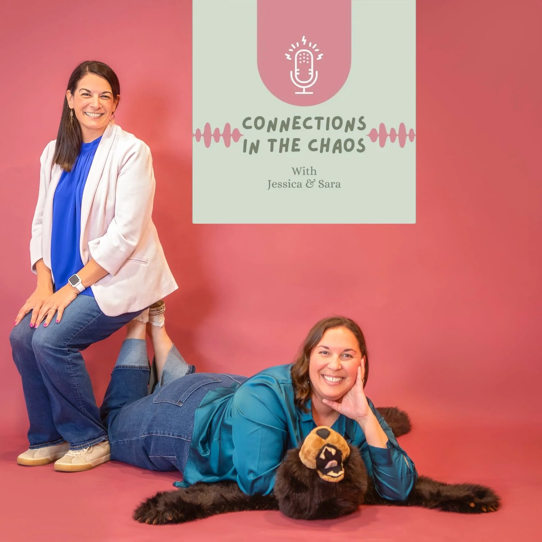 Three women playfully posing together with a large stuffed bear on a pink background. One woman is standing on the shoulders of another woman lying on the floor, while a third woman is curled up next to the bear, smiling and resting her head on her hand.