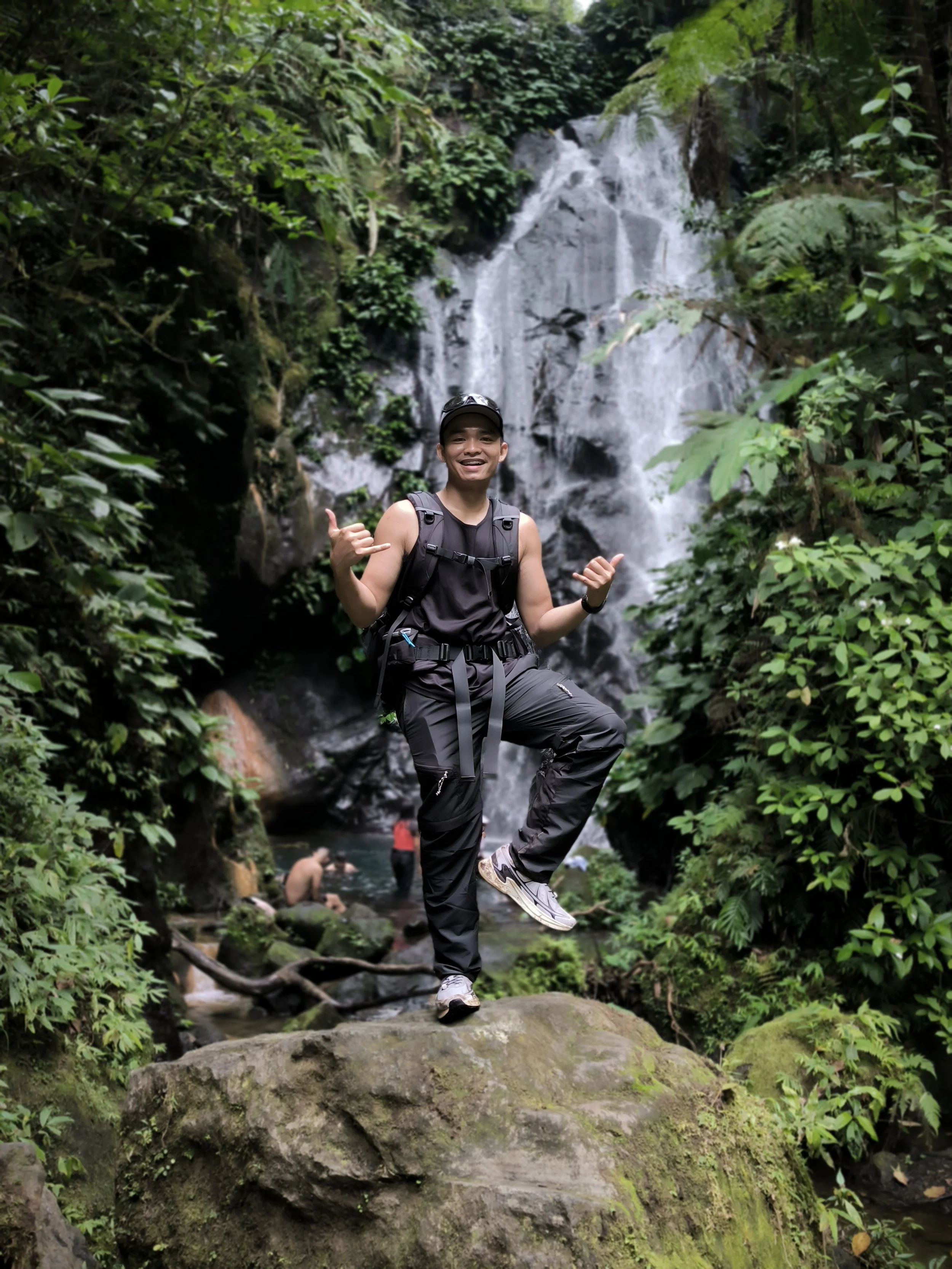 Hiker posing on a mossy rock in front of a jungle waterfall