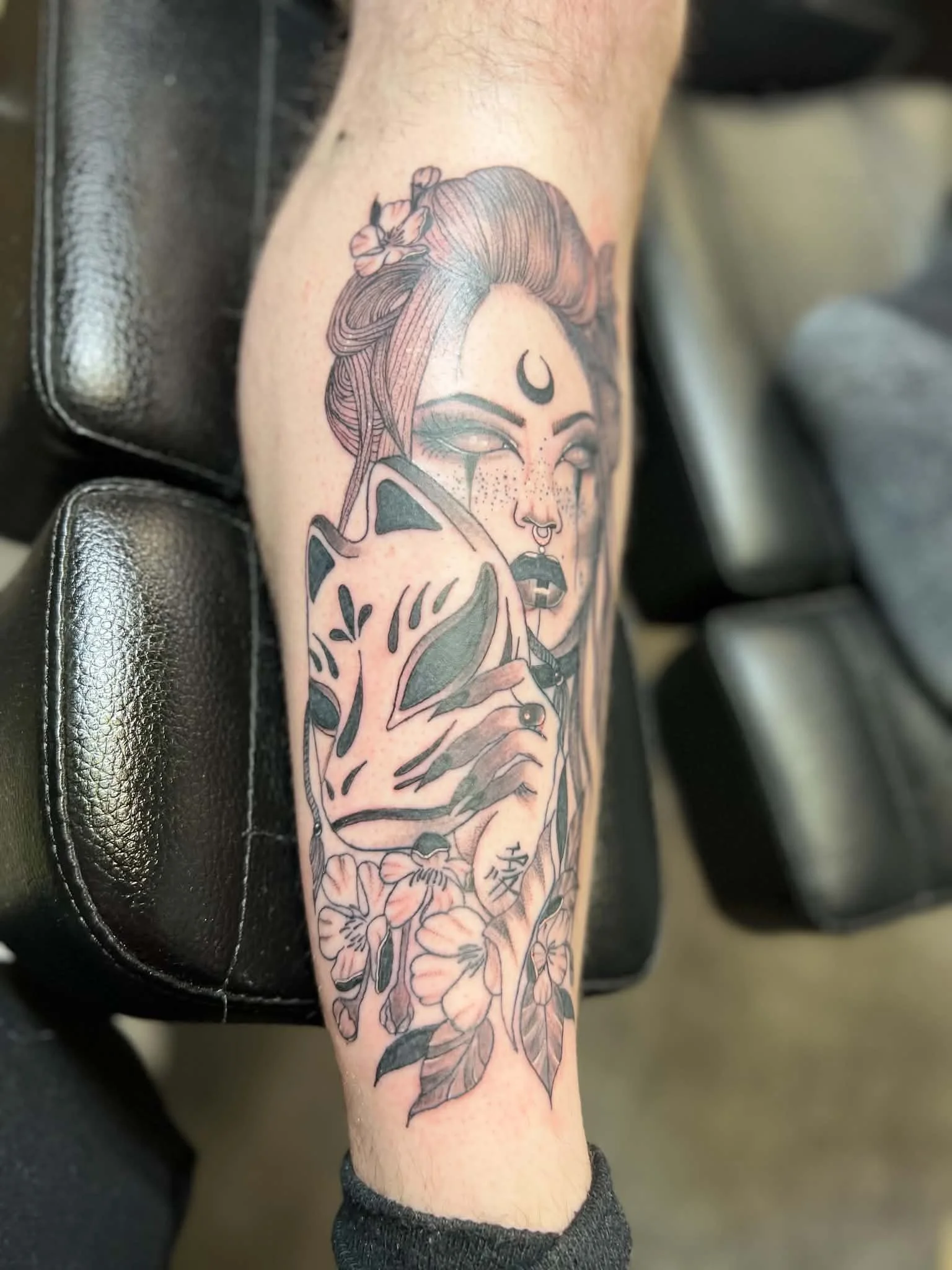 A tattoo of a woman with a crescent moon on her forehead, holding a sword, surrounded by flowers, on a person's forearm.