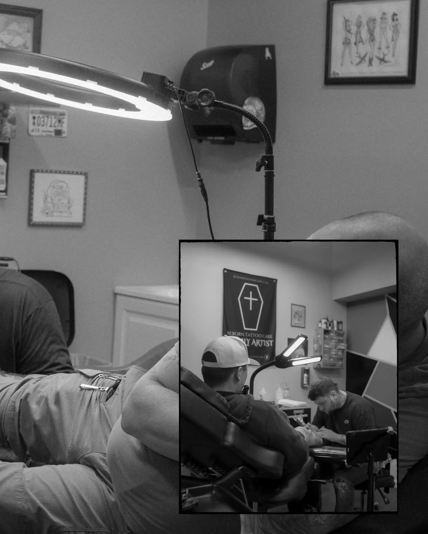A tattoo studio interior with a tattoo artist working on a client, posters on the wall including one with a coffin and cross, and professional lighting equipment.