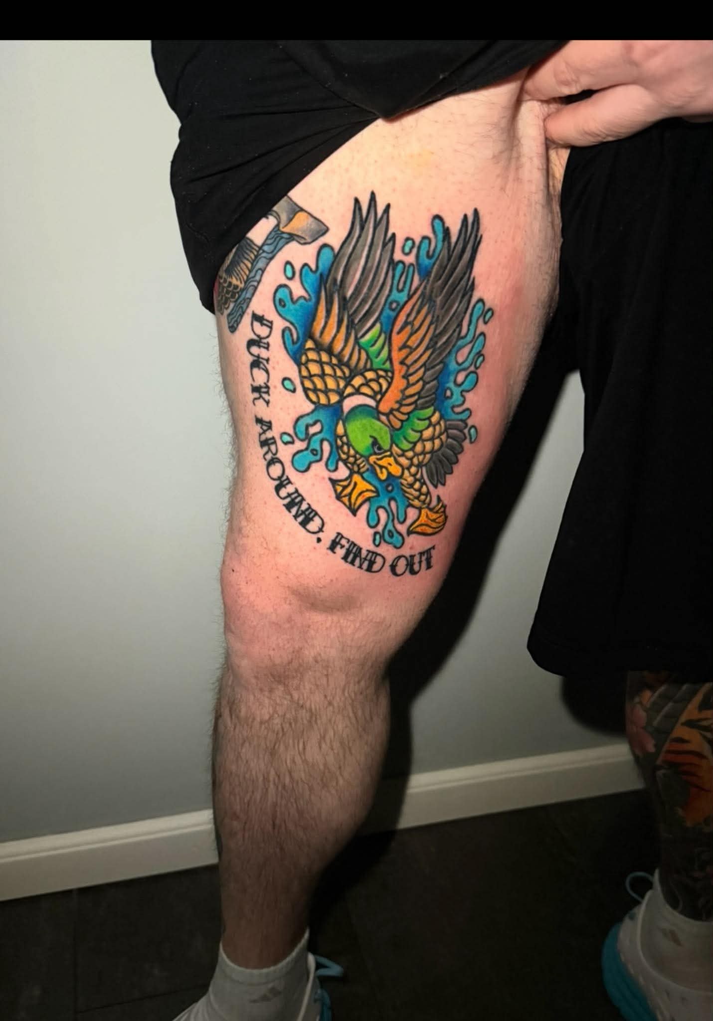 Tattooed upper arm and side of a person's torso, showing a colorful dragon and a blue splash design with black text.