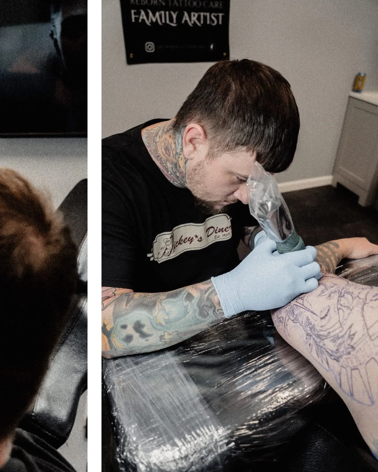 A tattoo artist with short dark hair, wearing a black shirt and latex gloves, is tattooing a design on a client's arm. The client has tattoos on their arm and is lying on a table covered with plastic. In the background, there is a black wall sign with text that reads 'FAMILY ARTIST', and a gray cabinet is visible.