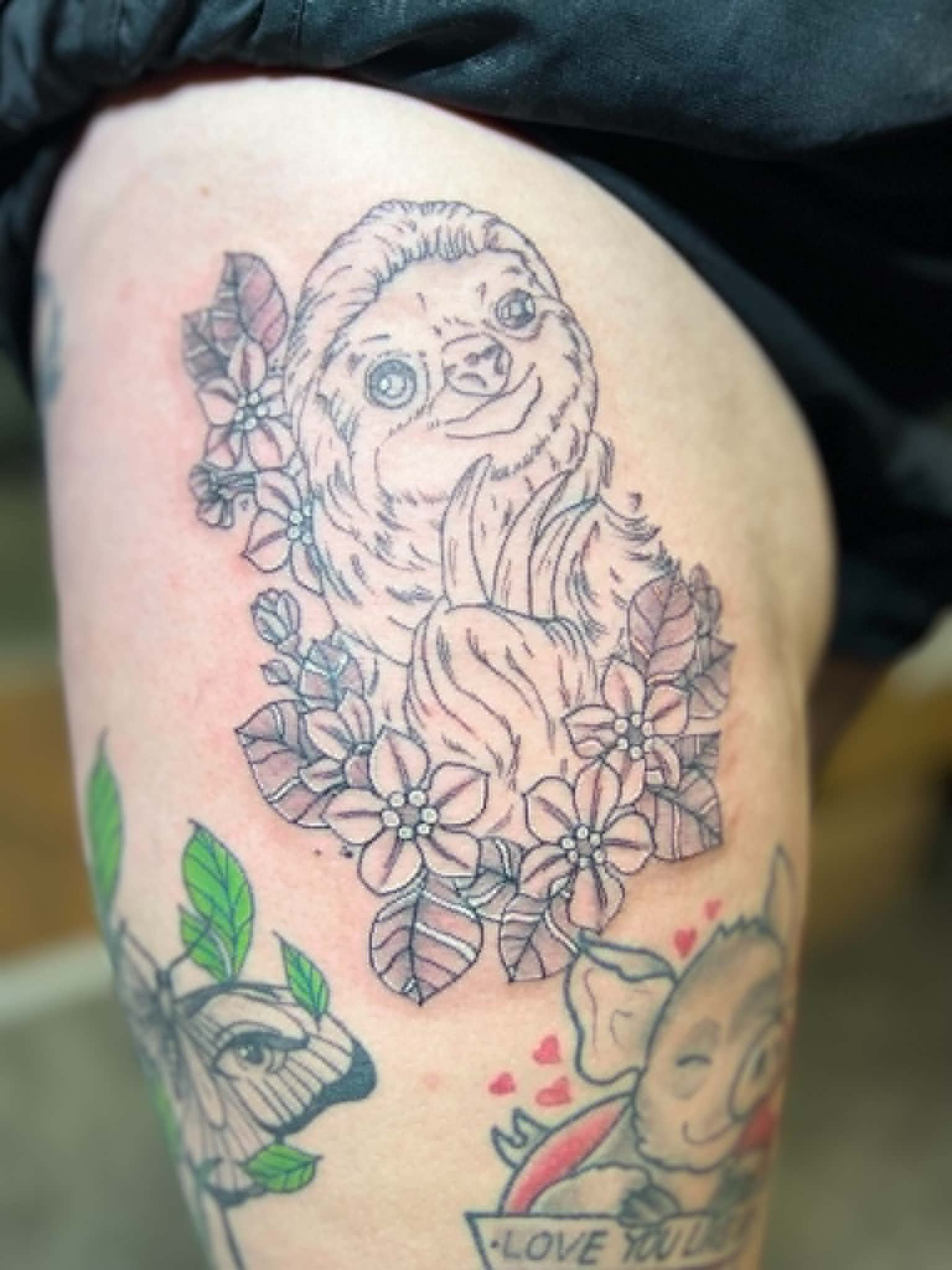 Tattoo of a sloth with glasses, surrounded by flowers and leaves, on a person's arm.