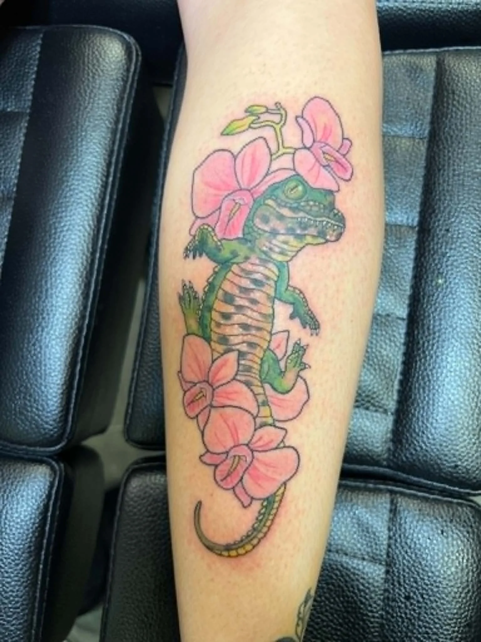 Colorful tattoo of a frog sitting among pink orchids on a person's arm.