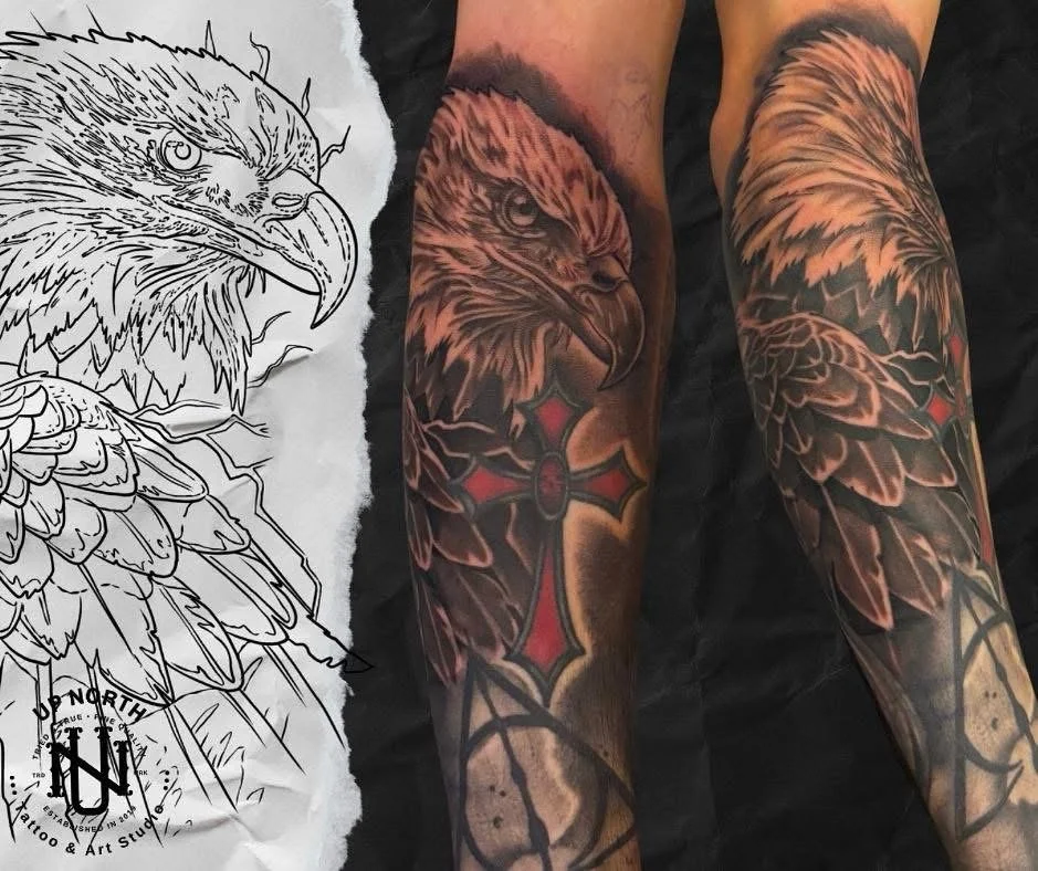 Close-up photo of a tattoo of an eagle's head with a red and black cross on the forearm, next to an outline of the same eagle design on paper.