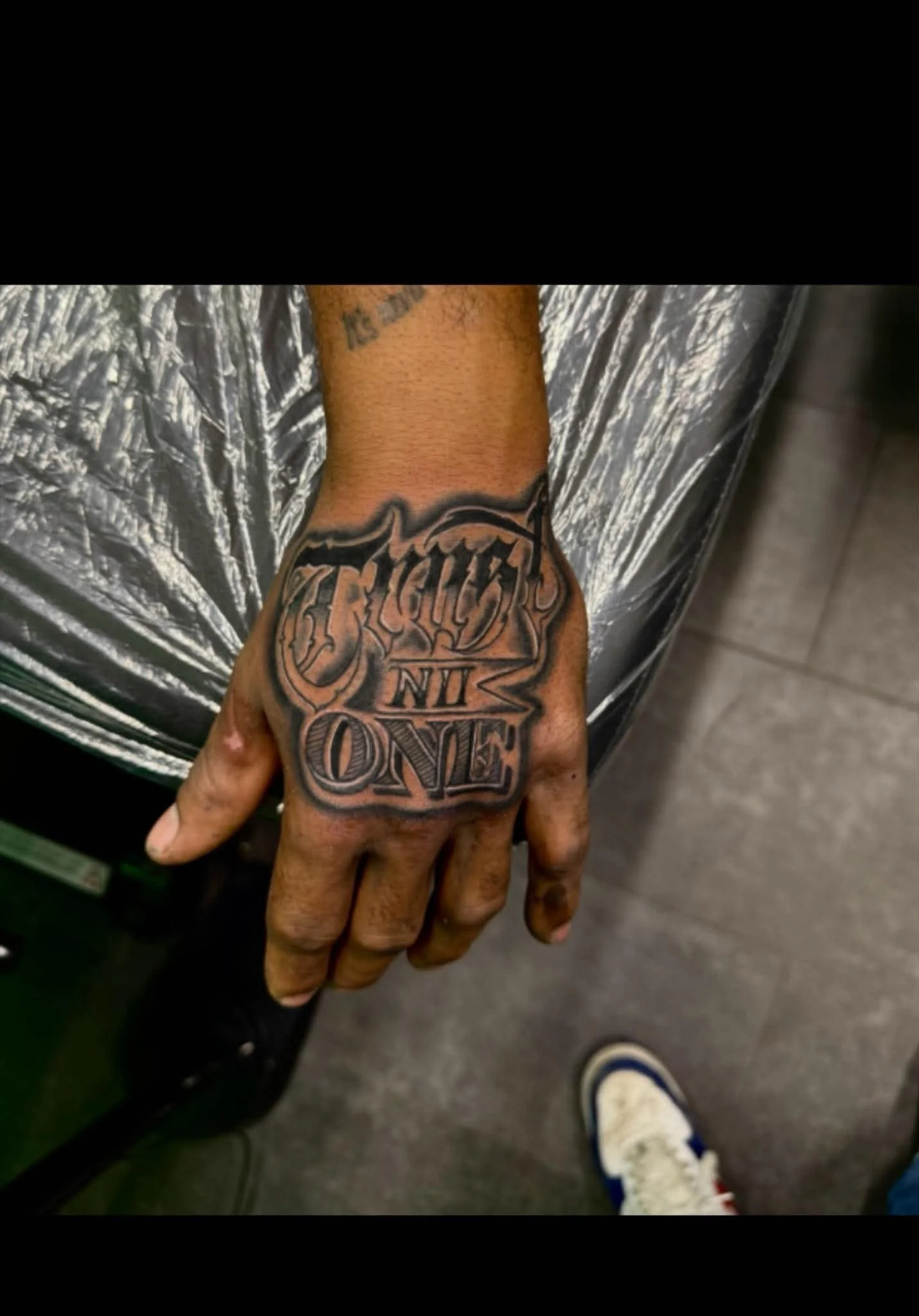 A person's hand with a large tattoo that says 'One' on the fingers and a word above that is partially visible and appears to say 'Respect' or 'Resist'