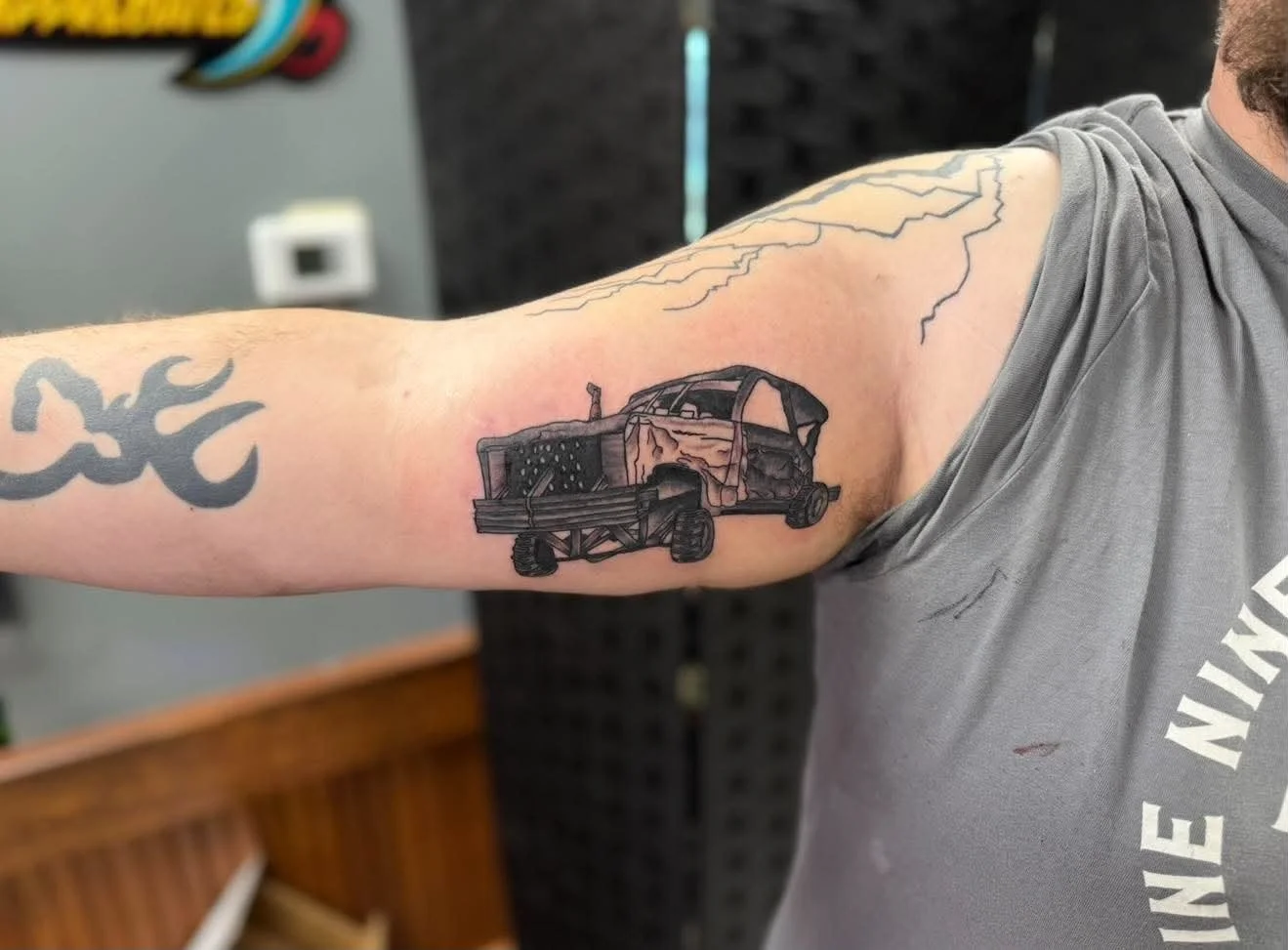 Tattoo of a damaged car on a person's upper arm, with some lightning bolt tattoos on the shoulder and upper arm.