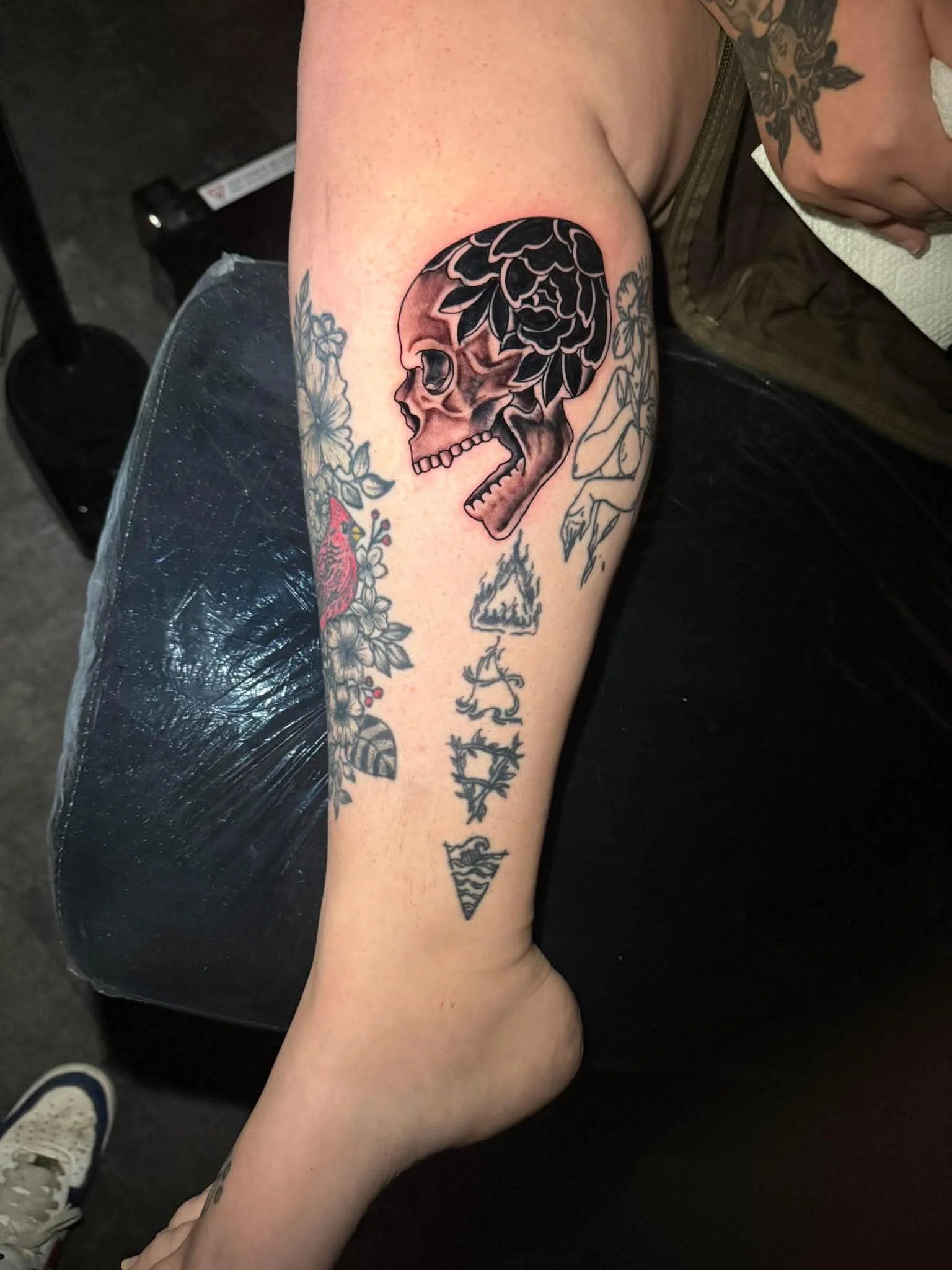 Tattoo of a skull with floral design on the skull's top and side, located on a person's upper arm.
