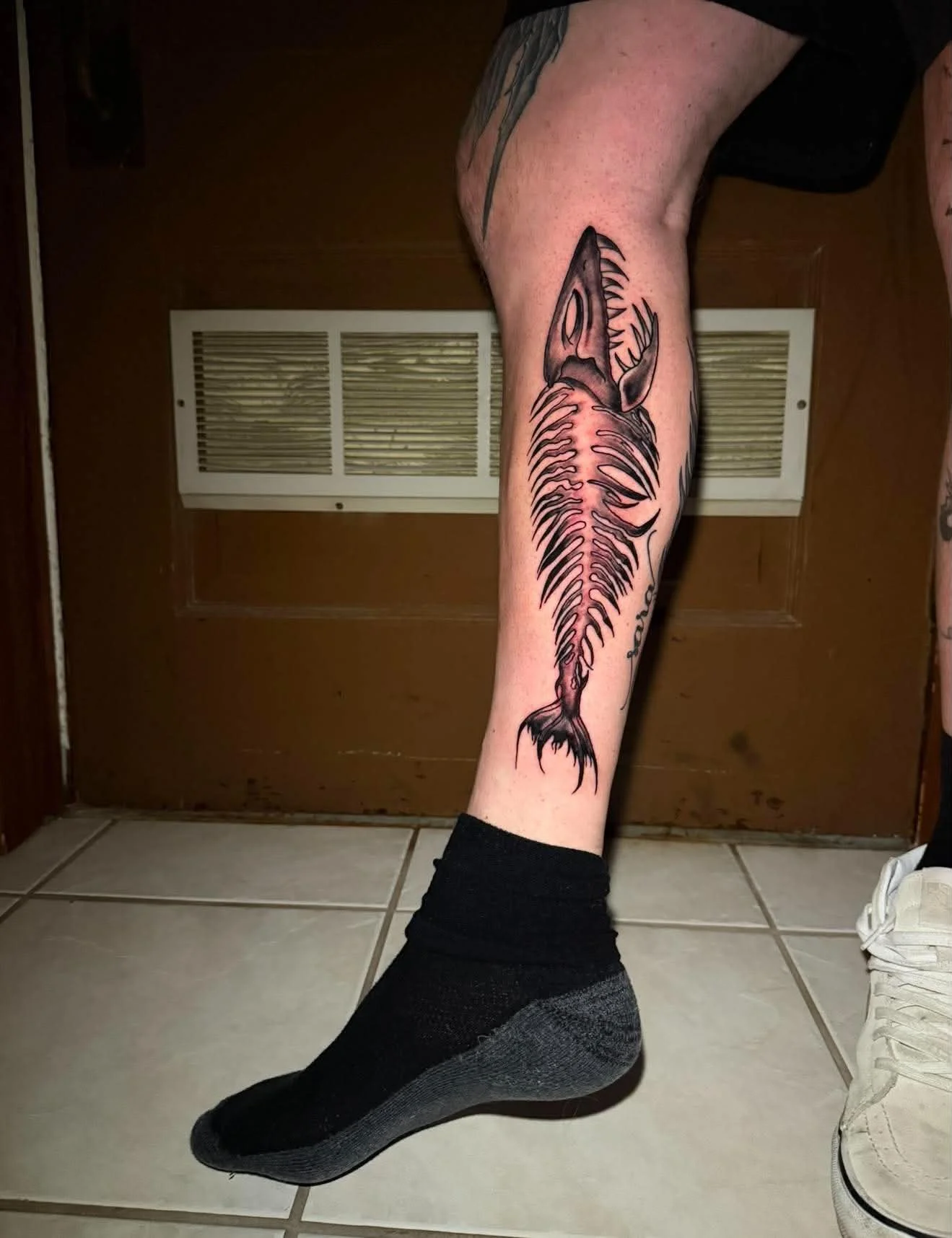 Tattoo of a fish skeleton on a person's leg.