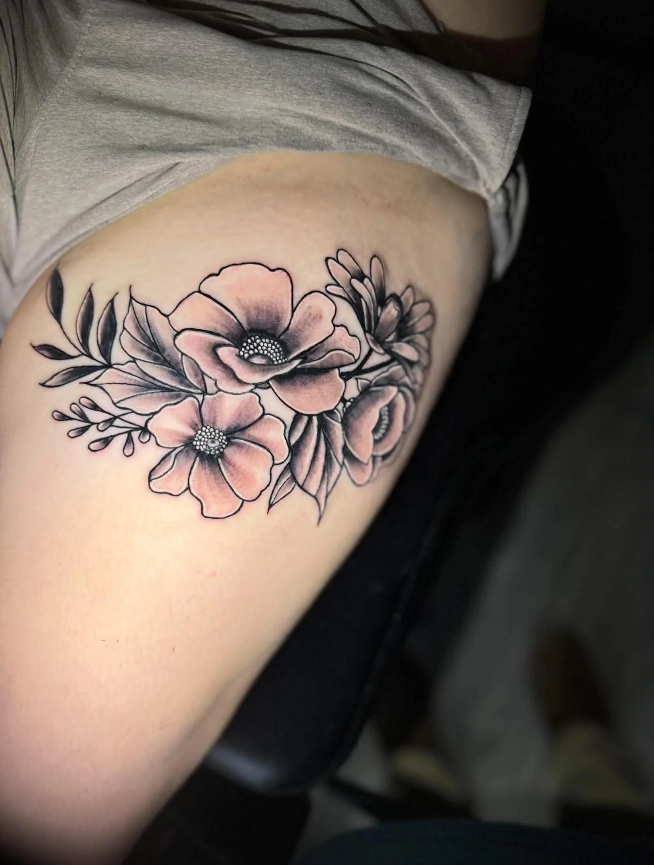 A floral tattoo on a person's upper arm featuring pink and black inked flowers with detailed petals and leaves.