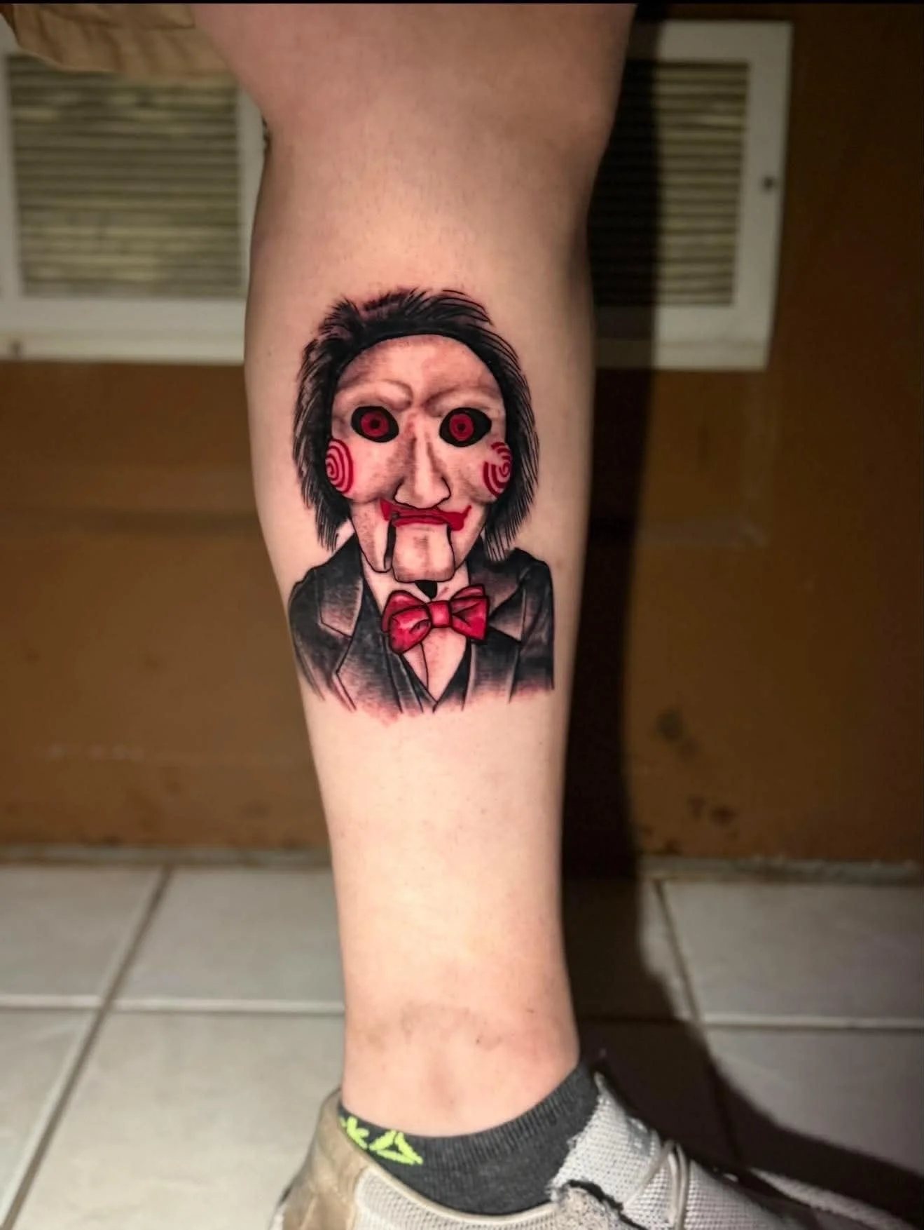 A tattoo of a creepy clown face on a person's leg.