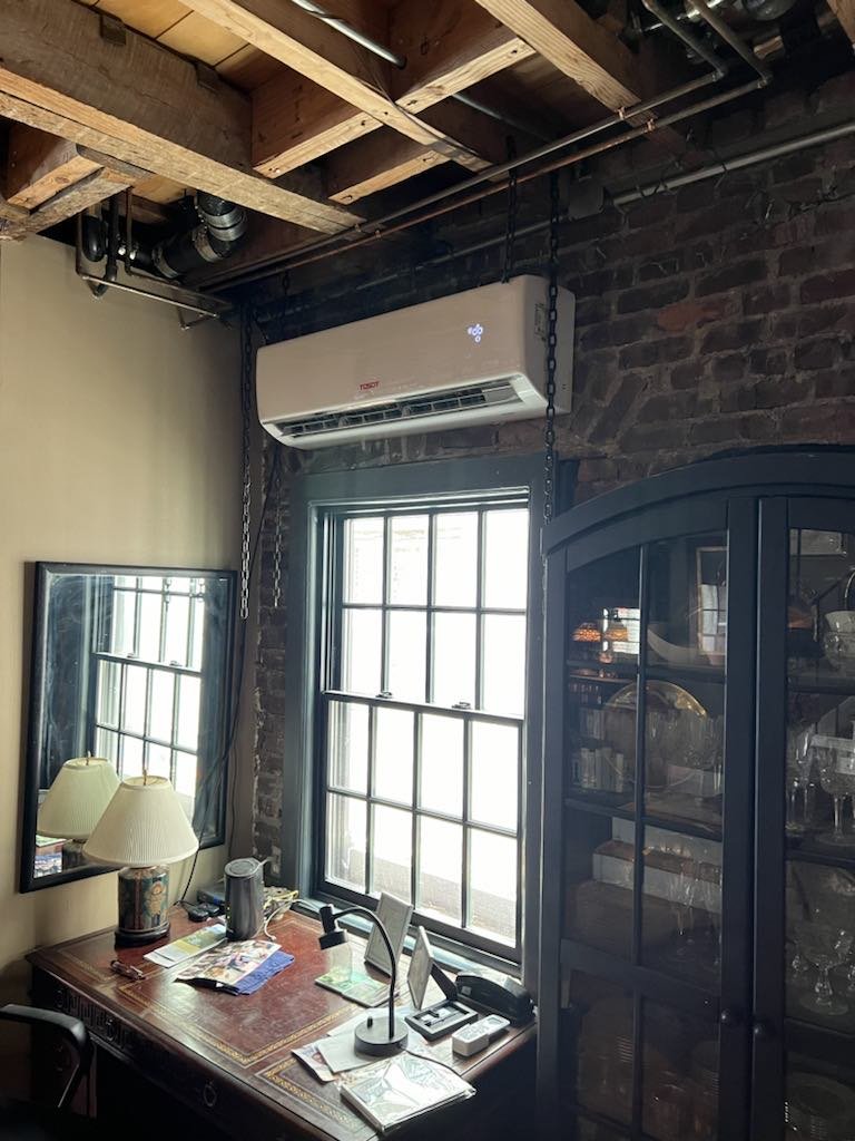 Living room with a wall-mounted indoor unit above a desk and brick wall