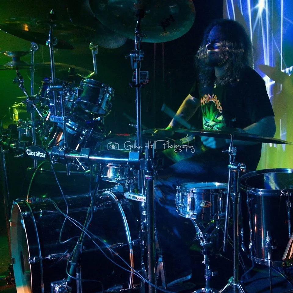 Drummer playing a drum set on a stage with colorful lighting.