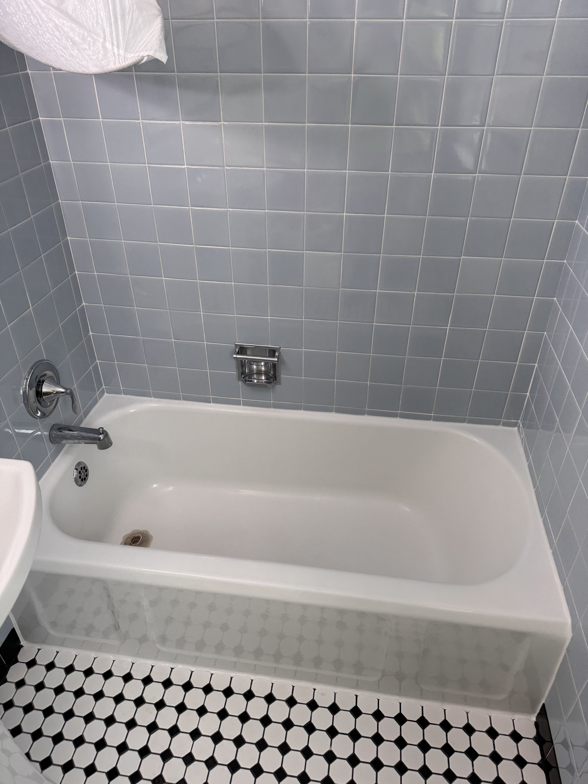 A bathtub with a mosaic tile floor underneath and a gray tiled wall behind it, with a silver faucet and drain visible.