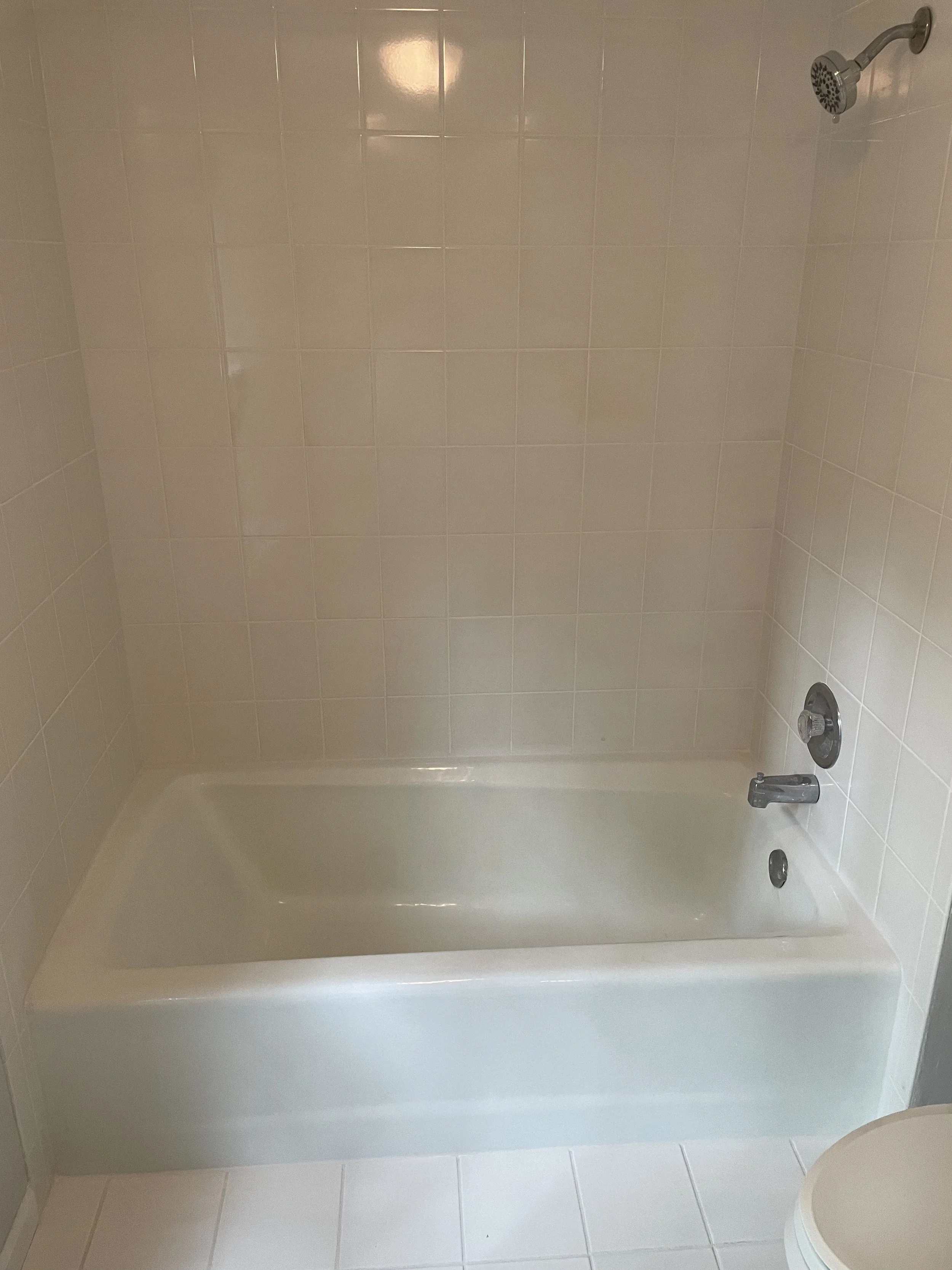 A plain bathtub with beige tile walls and floor, a showerhead mounted on the wall, a faucet, and a drainage drain.