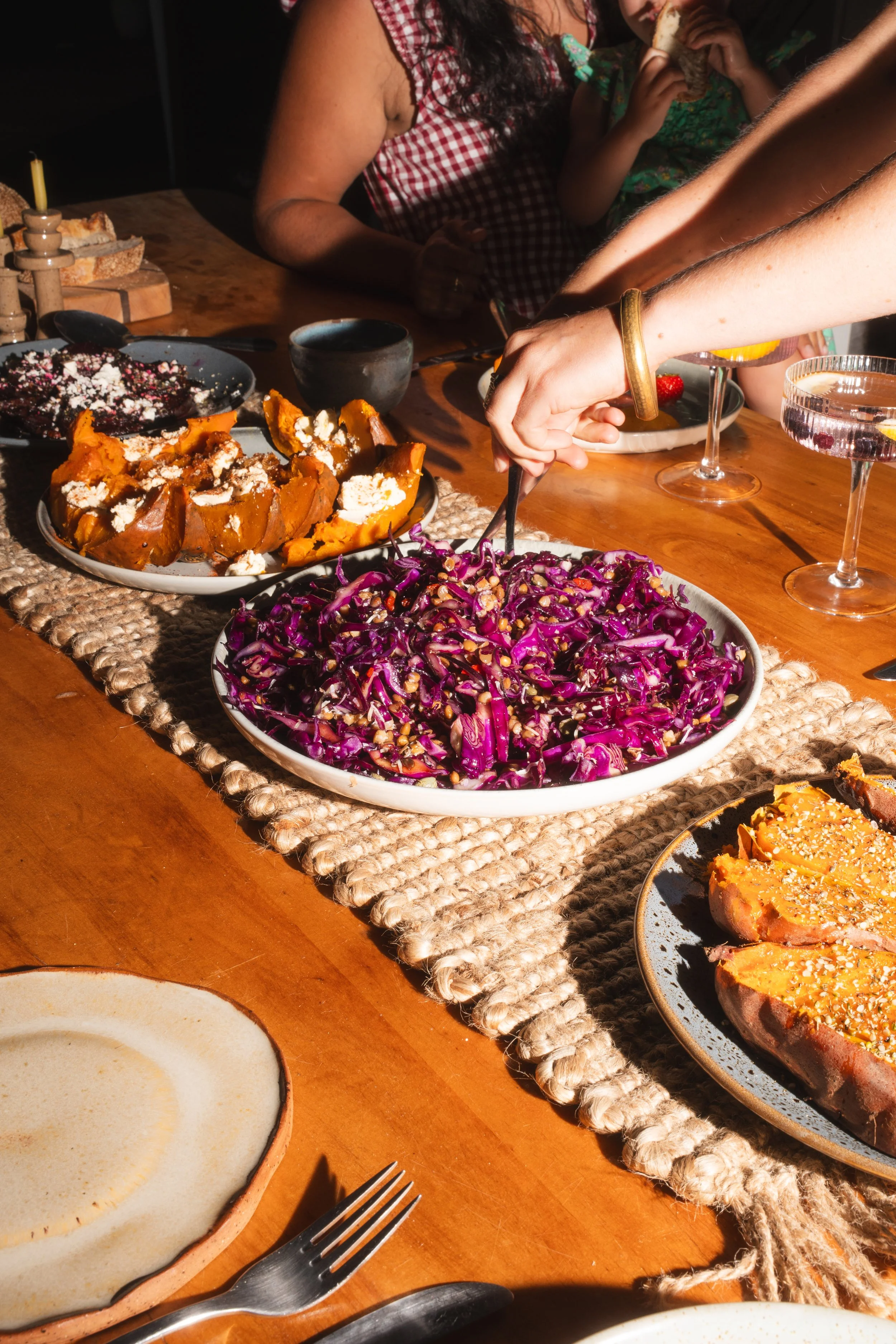 A table of food including purple cabbage salad with nuts, roasted pumpkin, and other dishes, with people around the table serving themselves.