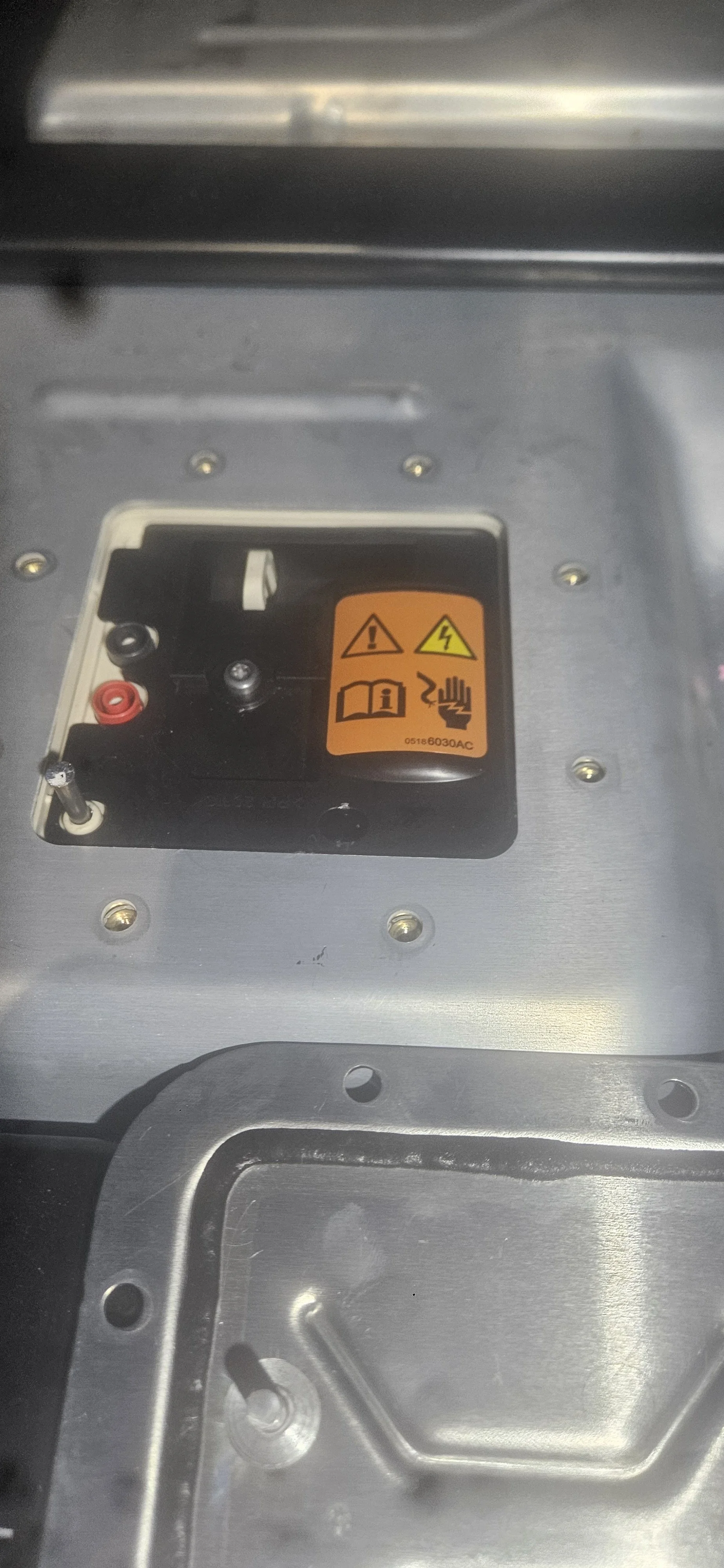 Close-up of an electrical panel with warning and instruction labels, showing terminal connections and mounting screws.