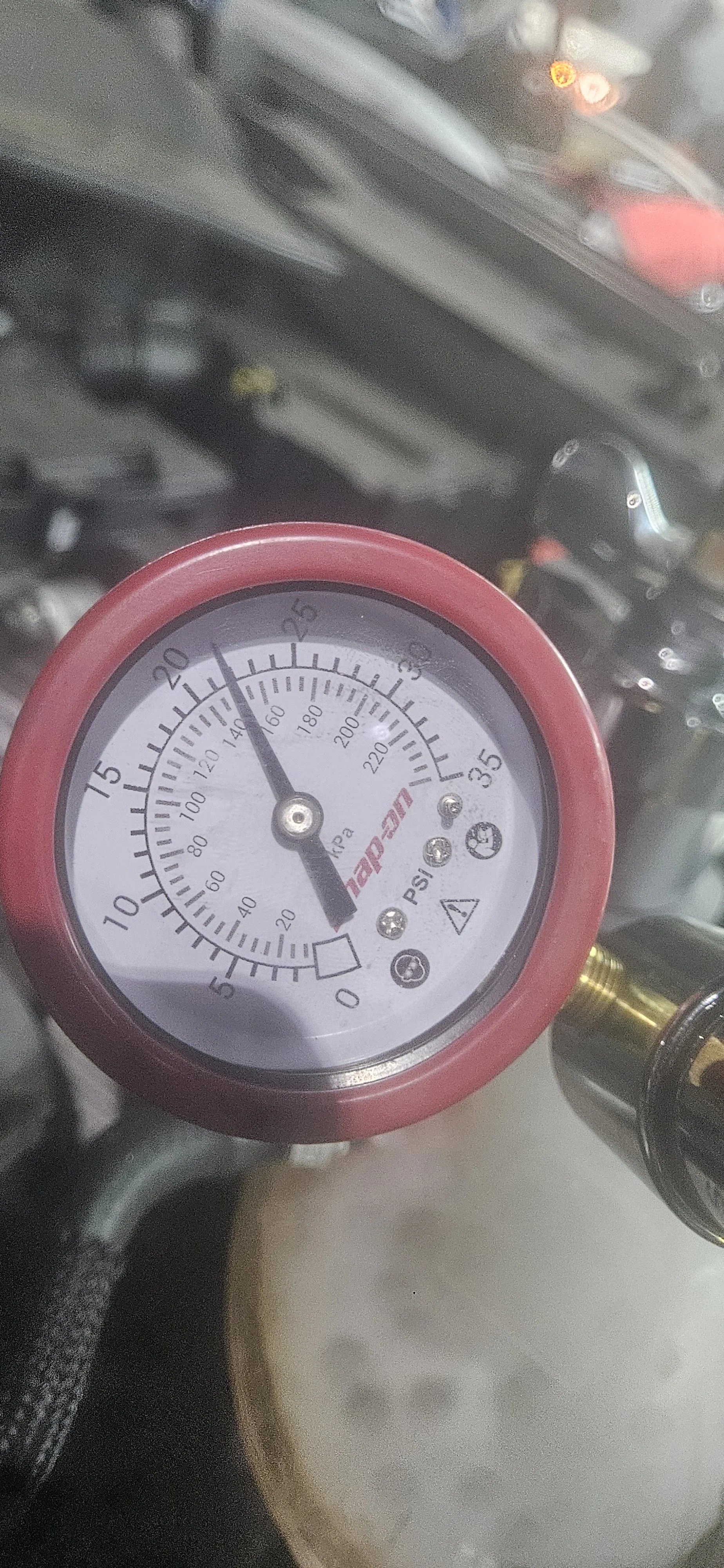 A pressure gauge displaying a reading of approximately 125 psi, with a red casing and brand logo 'TECDAP' on the dial, mounted on a mechanical device.