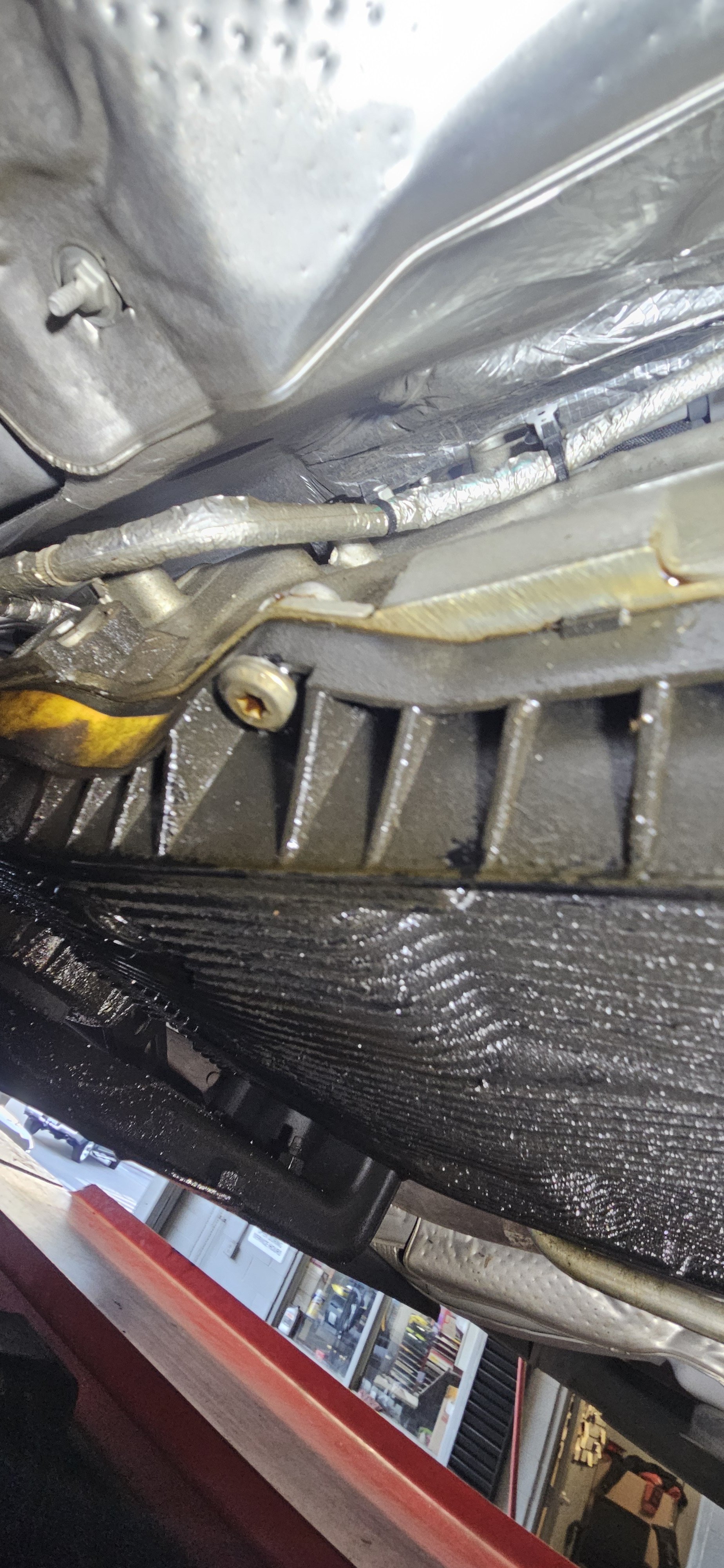 Close-up view of the underside of a vehicle showing part of the engine with oil and grime, and some metallic components and a plastic oil pan.