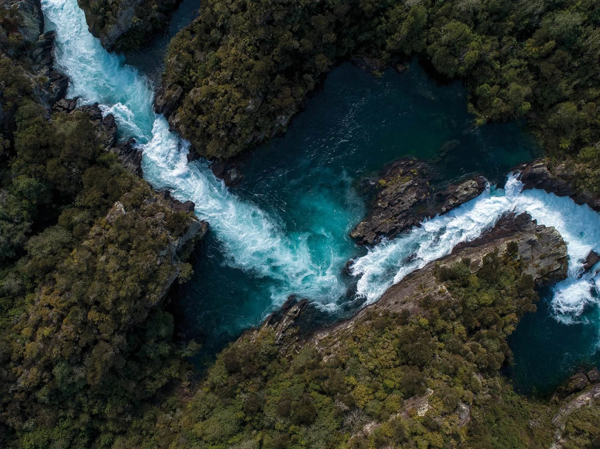 Aerial view of a winding river flowing down the Aratiatia Rapids, through a dense forested landscape with rocky banks.