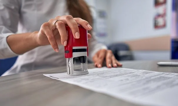 Person using a red stamp to mark a document on a desk.