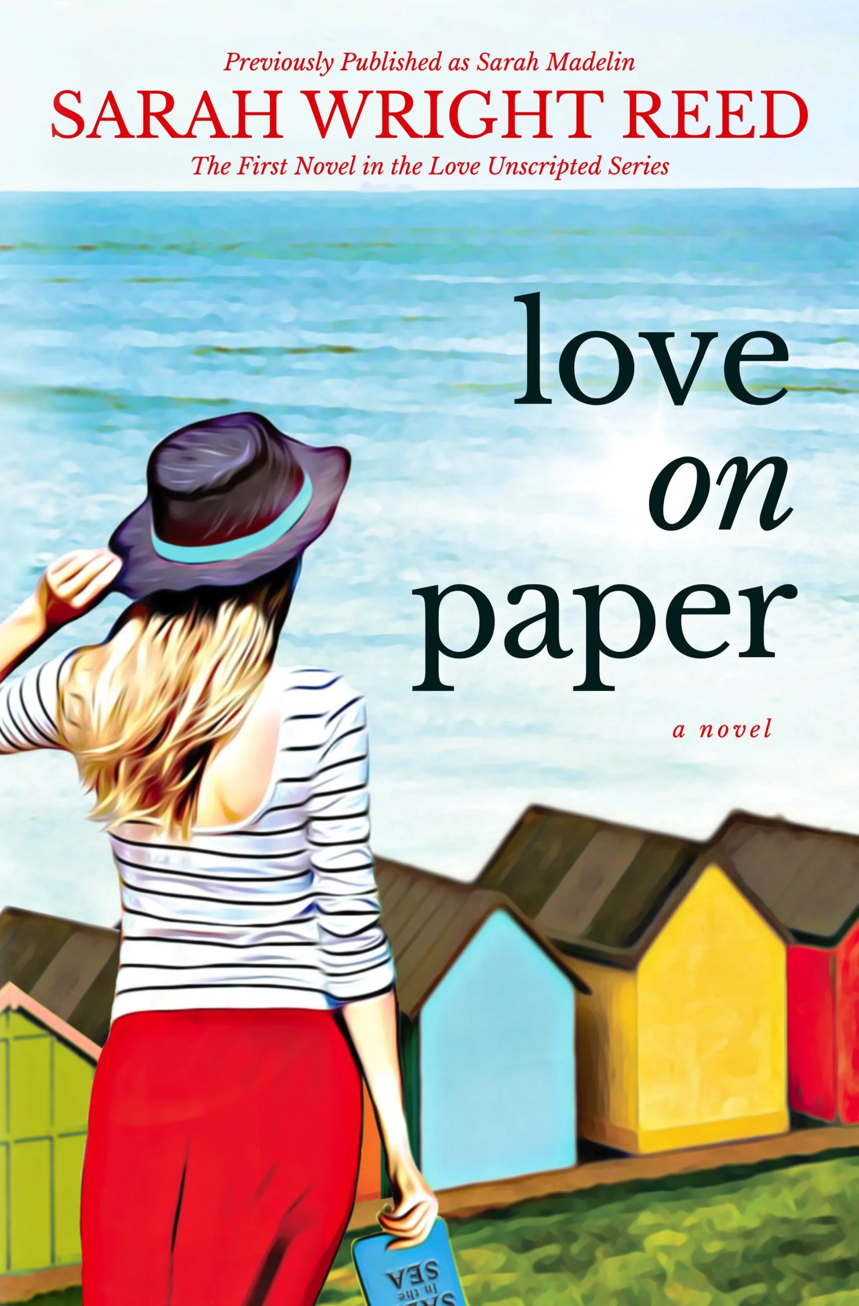 Book cover titled "Love on Paper" by Sarah Wright Reed. It features a woman with long hair, wearing a striped shirt, red pants, and a wide-brimmed hat, standing on a grassy area near colorful houses. She holds a sign that reads "Sea" and appears to be looking at the houses.