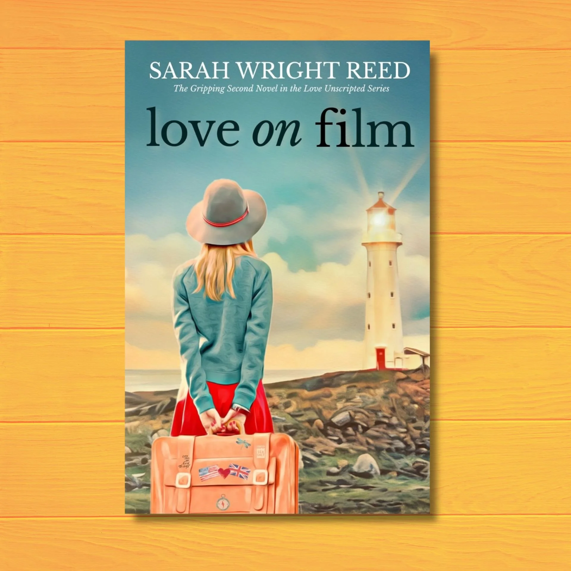 Cover of the book 'Love on Film' by Sarah Wright Reed, depicting a girl standing on a rocky shore holding a suitcase decorated with stickers, including flags of the United States and the United Kingdom, with a lighthouse and a sunset in the background.
