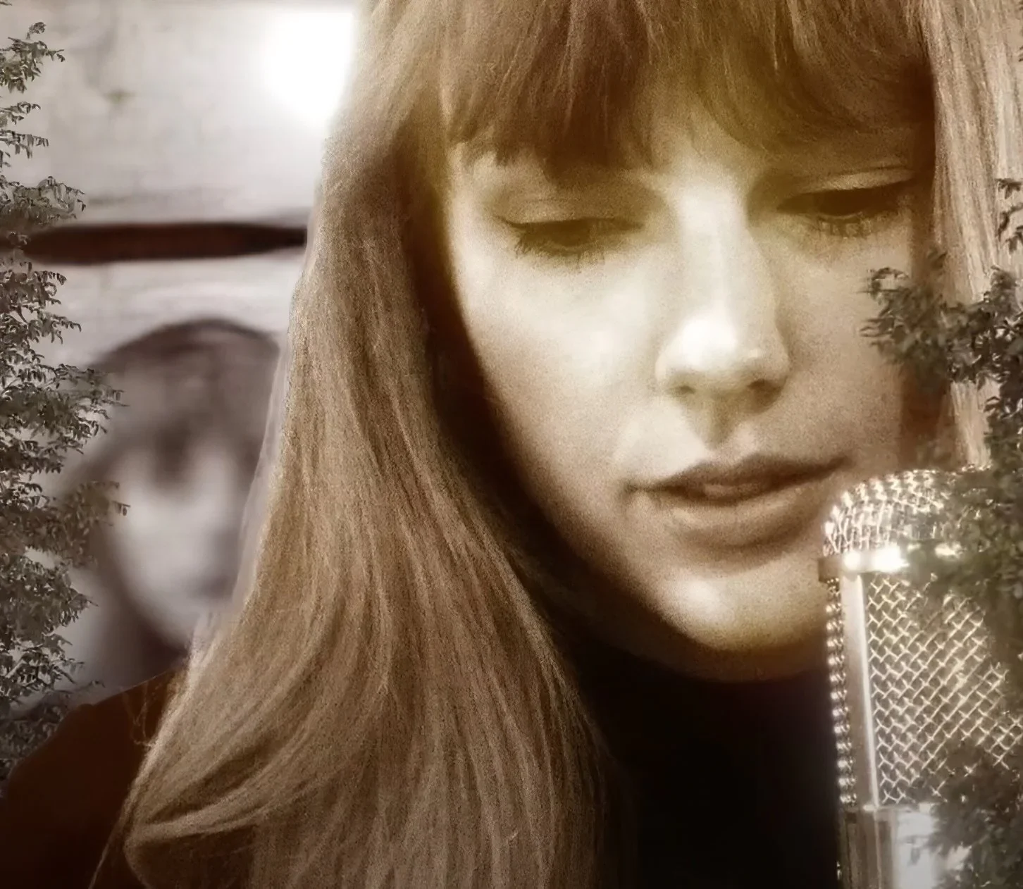 A woman singing or speaking into a vintage microphone, with trees in the background.
