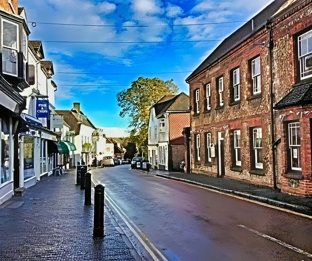 A quiet street in a small town with shops and buildings, under a blue sky with scattered clouds.