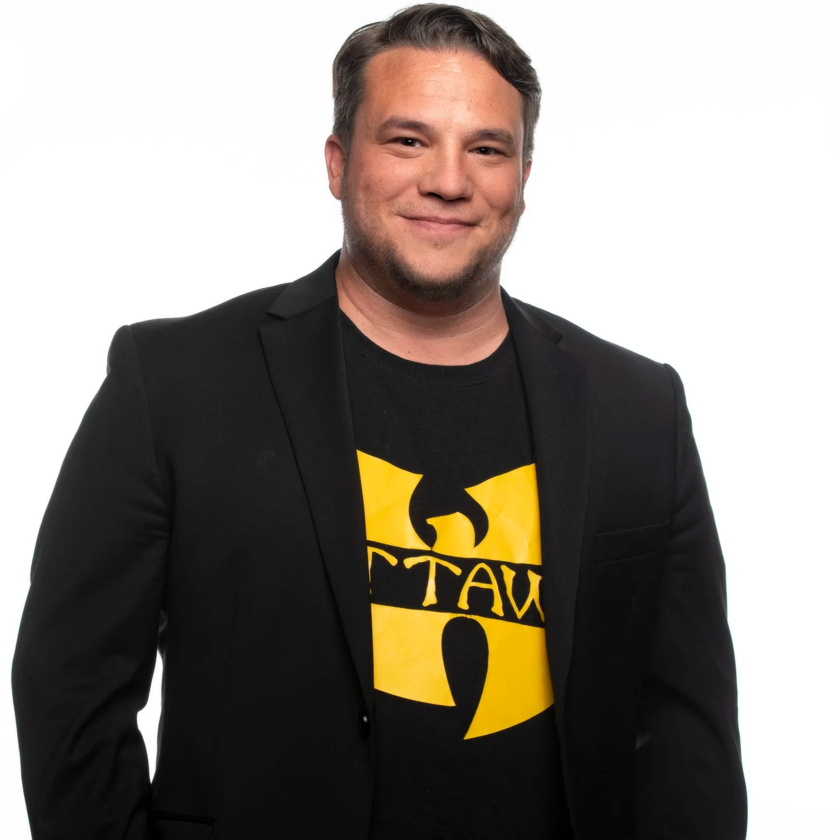 Matt Luloff wearing a black blazer over a black shirt with yellow text, smiling against a white background.