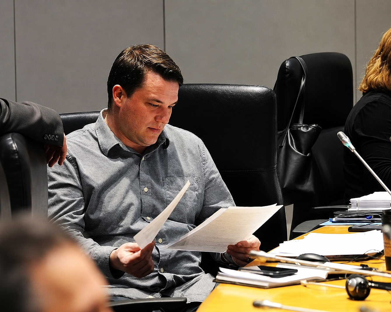 Matt Luloff in a gray shirt reading a document at a desk in a conference room.